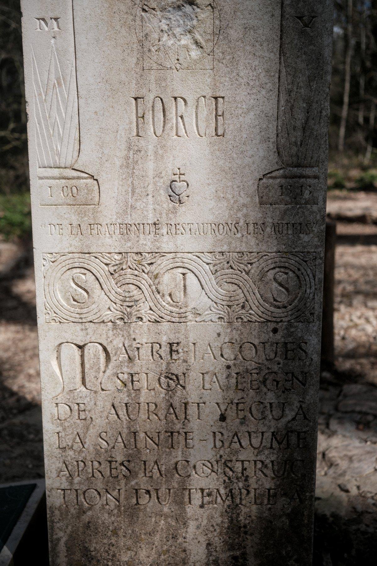 Photo verticale. Une pierre lisse gravée de multiples inscriptions et d’ornements. Le mot FORCE est mis en avant en haut, au centre, entre 2 colonnes en gravure