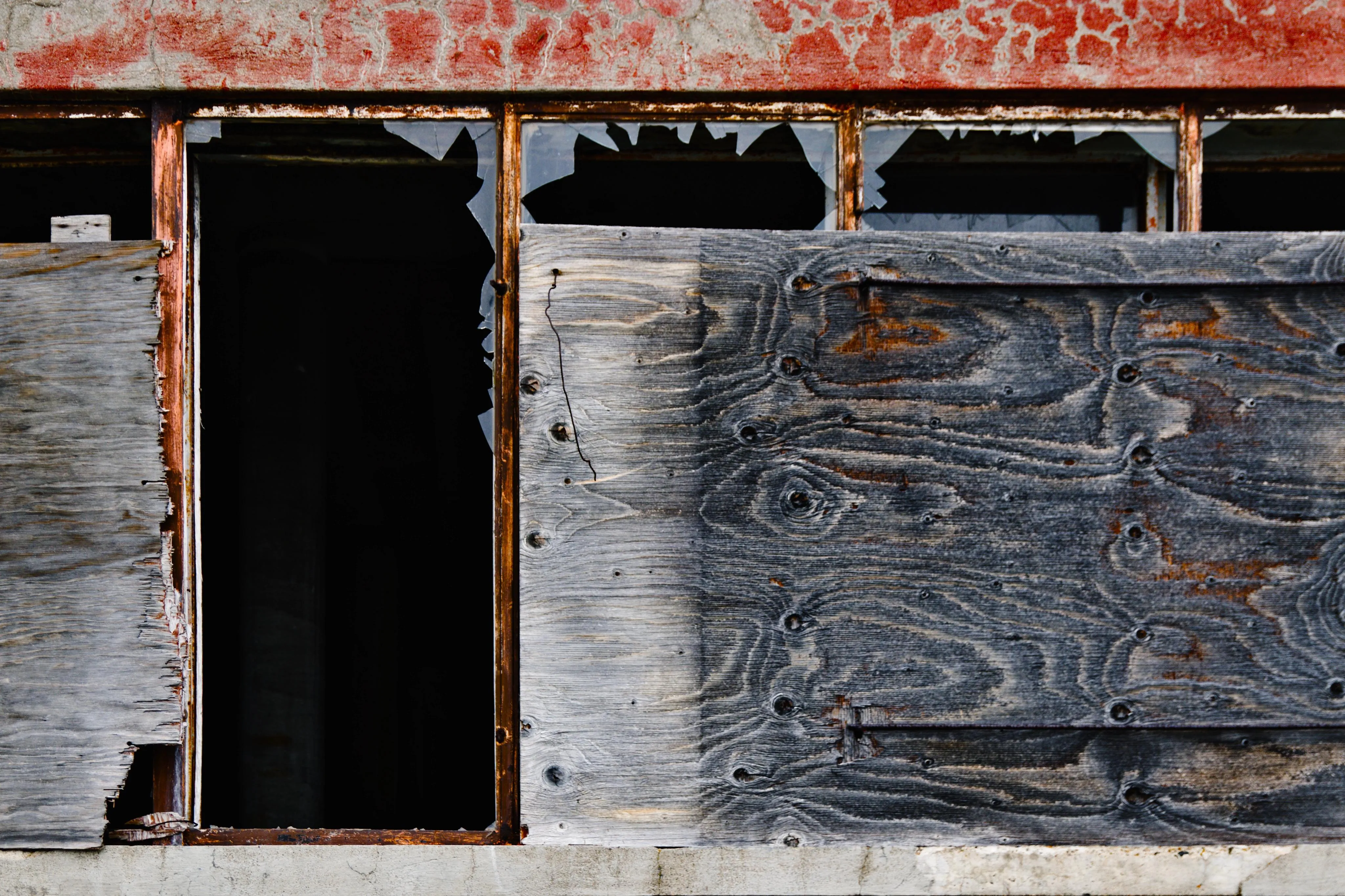 Broken windows of an abandoned building. Part of it has been blocked with wooden panels.