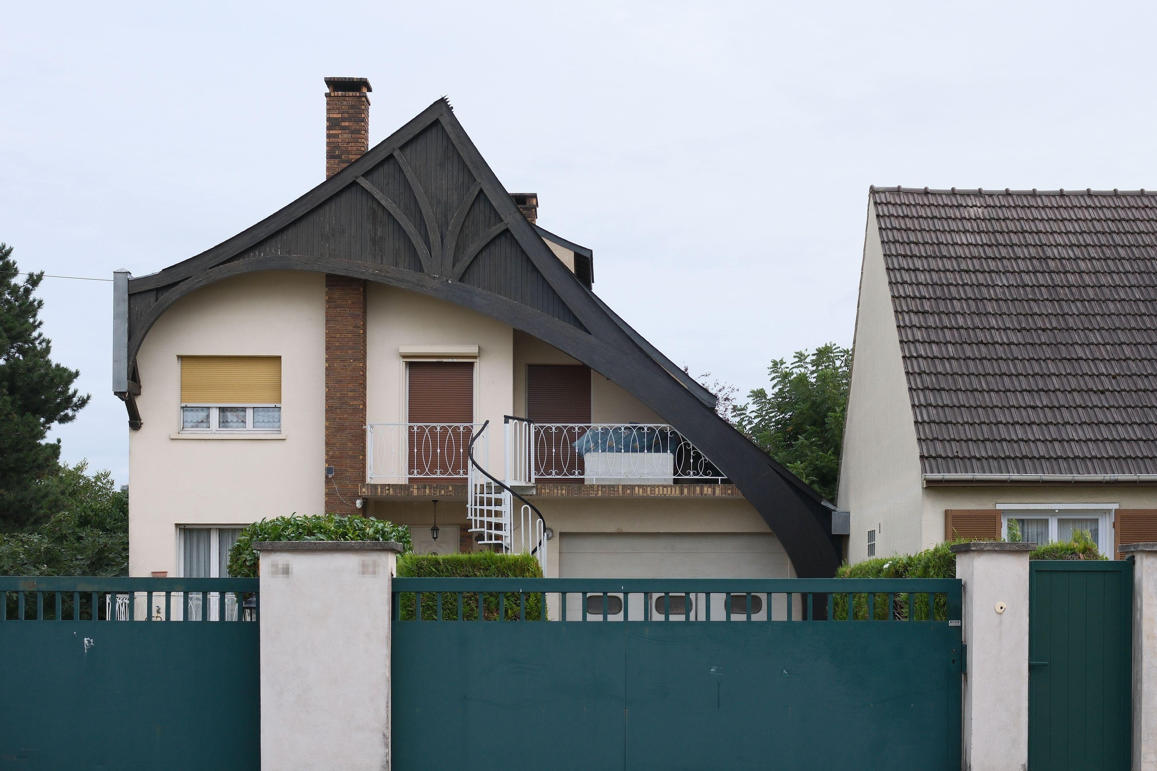 Photo horizontale. Une maison dont le toit est original, asymétrique et dont le côté droit se prolonge en plongeant vers le sol