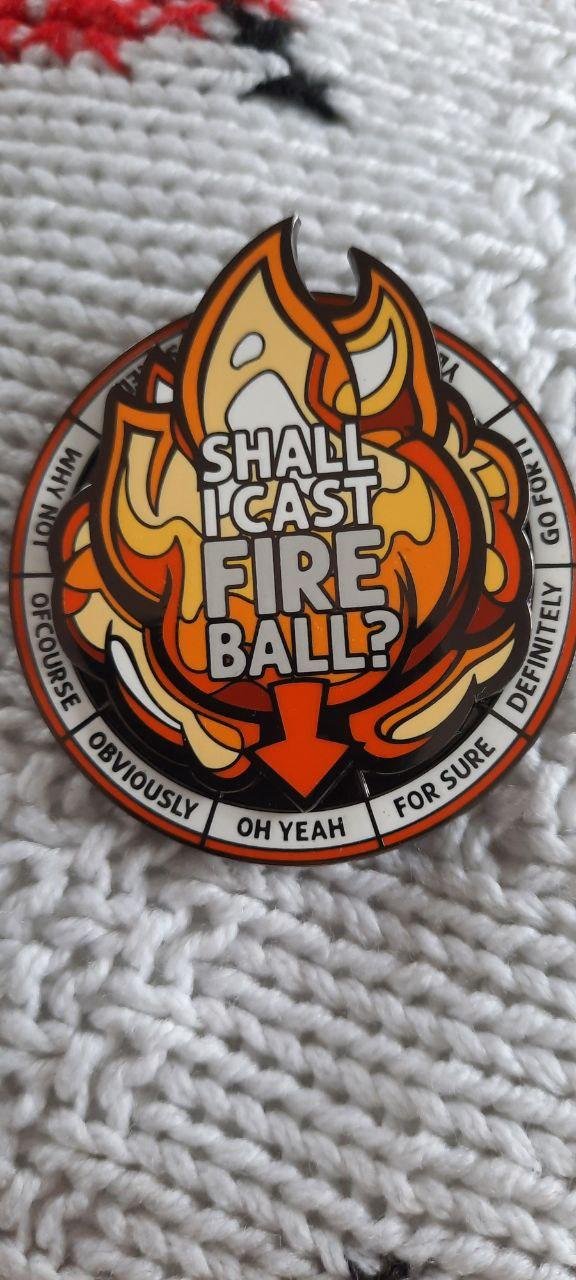 The image shows a circular, decorative spinner with text related to casting a "Fireball" spell. It asks, "Shall I cast Fireball?" with various affirmative responses around the edge, such as "OH YEAH," "OF COURSE," "OBVIOUSLY," "FOR SURE," and "DEFINITELY." It's likely a playful item for decision-making or humor.