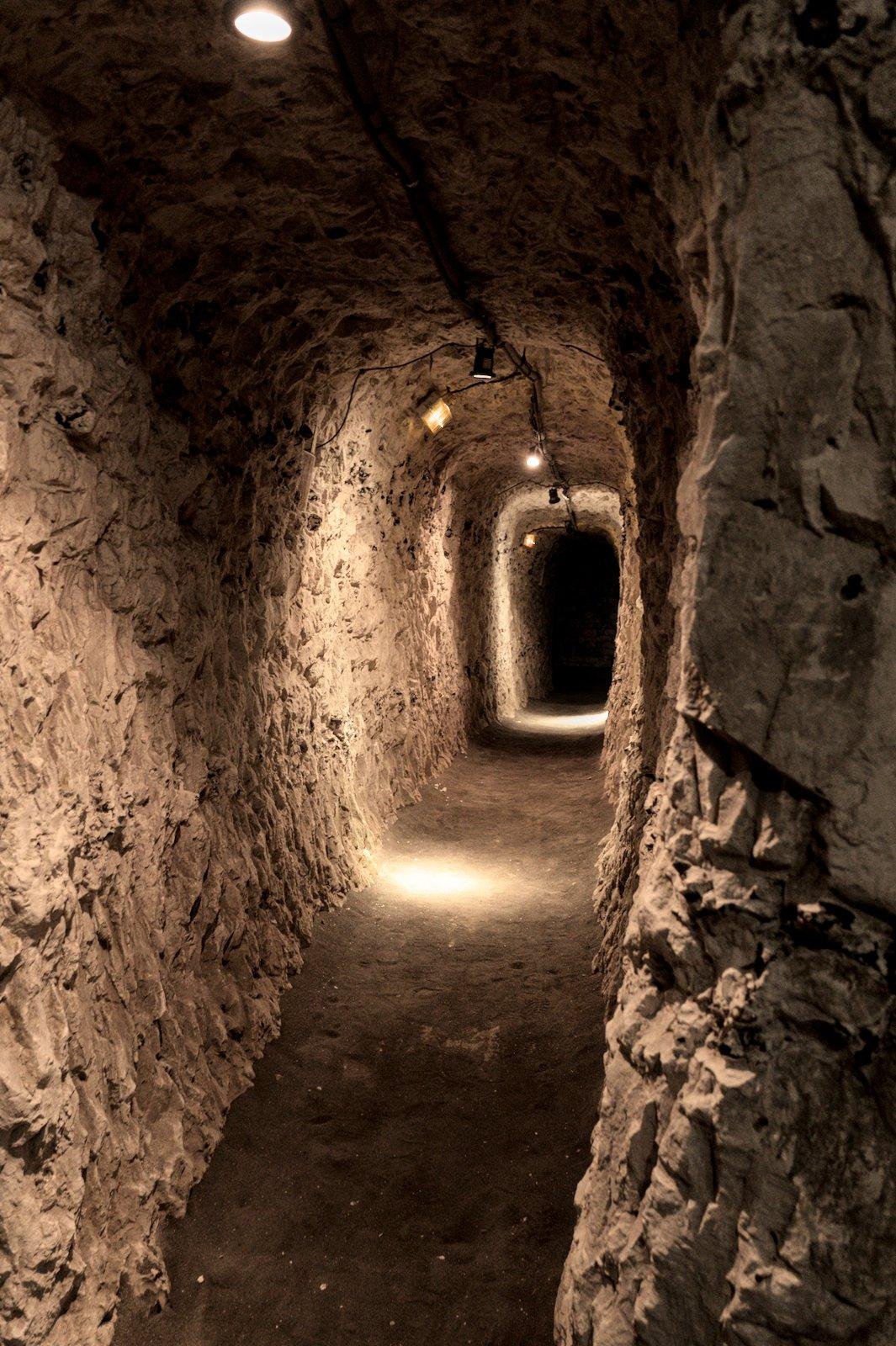 Photo format portrait d’un tunnel creusé à même la pierre avec des lampes disposées à intervals réguliers, formant des bulles de lumières orange tout le long