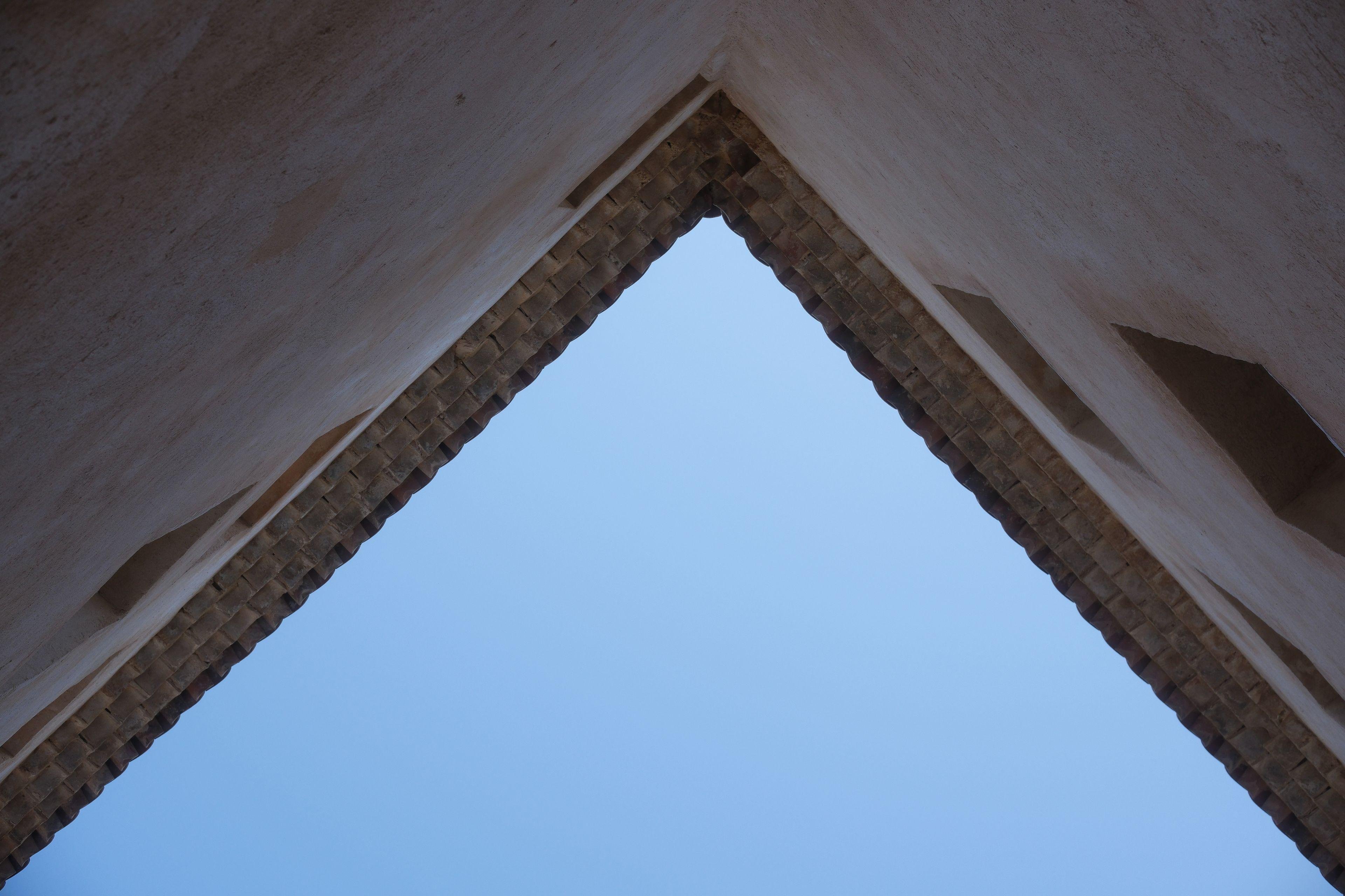 Photo d’un angle de mur vers le ciel, formant 1 triangle bleu et presque 2 autres triangles fait de mur