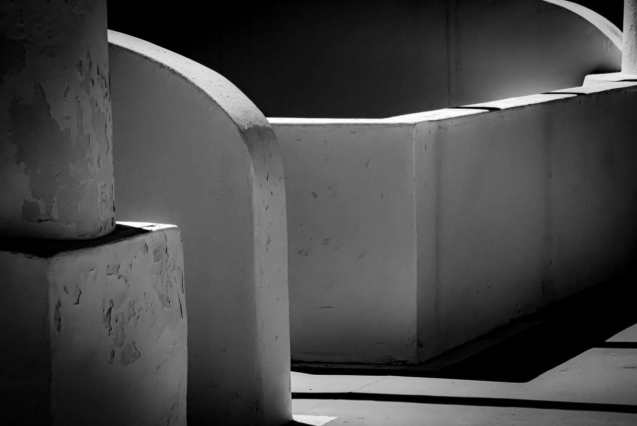 Curved concrete walls and columns in black and white, with strong sunlight casting deep shadows across the smooth surfaces and floor.