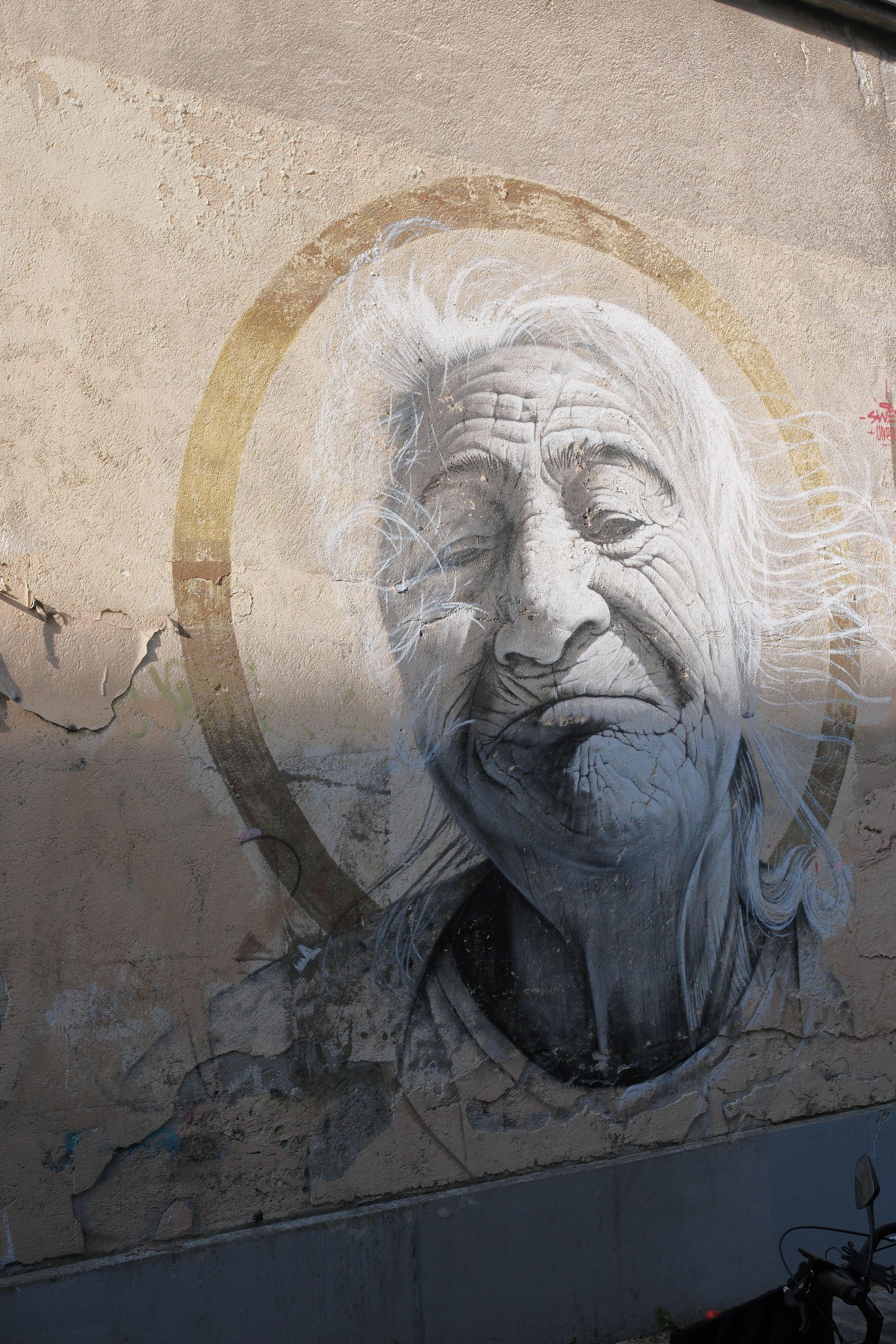 Picture of a big street painting depicting an old Native American, smiling in a comforting manner, looking gently down on us, surrounded by a golden circle