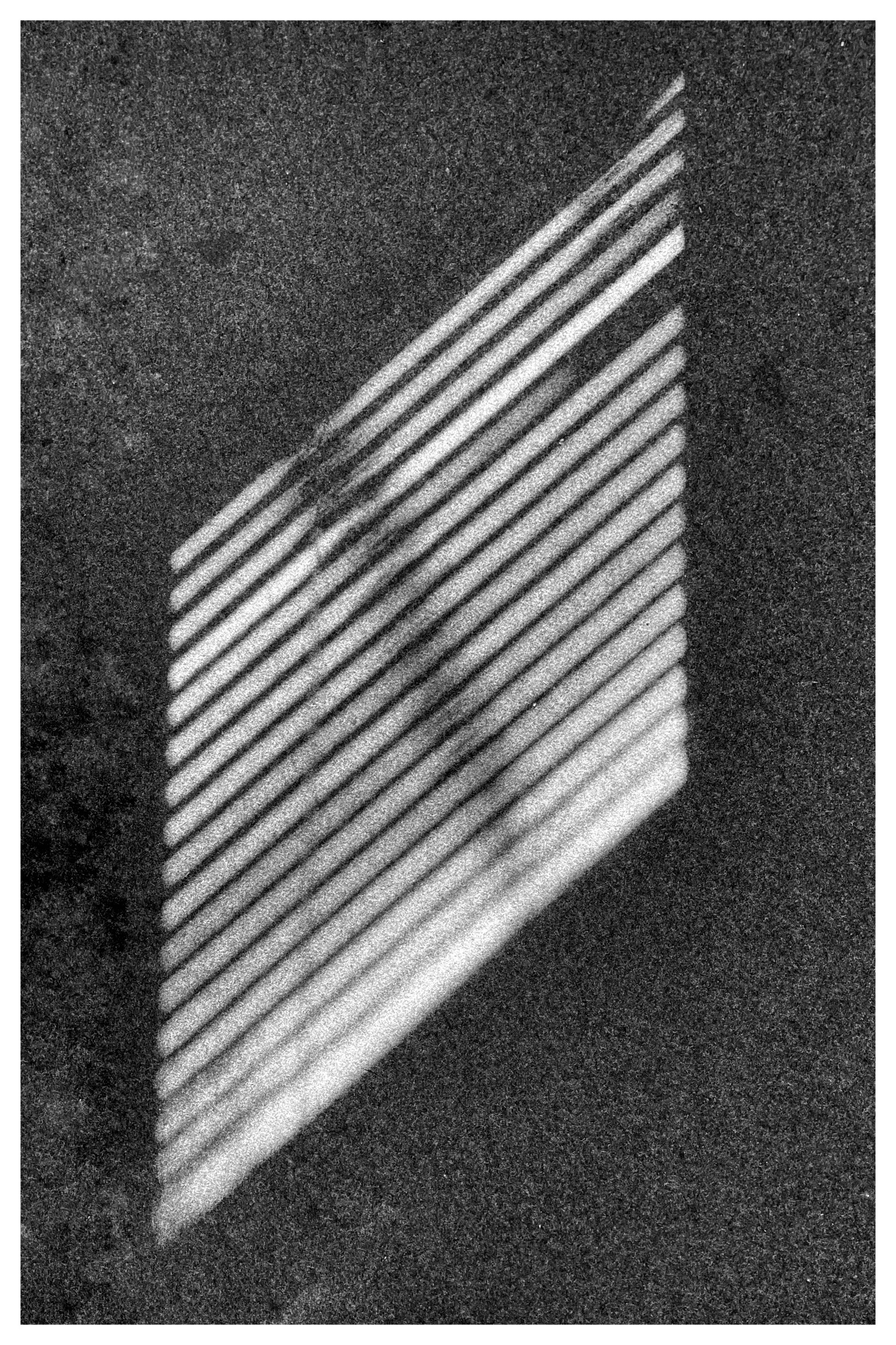 Diagonal striped shadows cast on a textured surface, forming a rectangular pattern of parallel lines varying in intensity from light to dark. The surface has a grainy appearance, enhancing the contrast of the shadows.