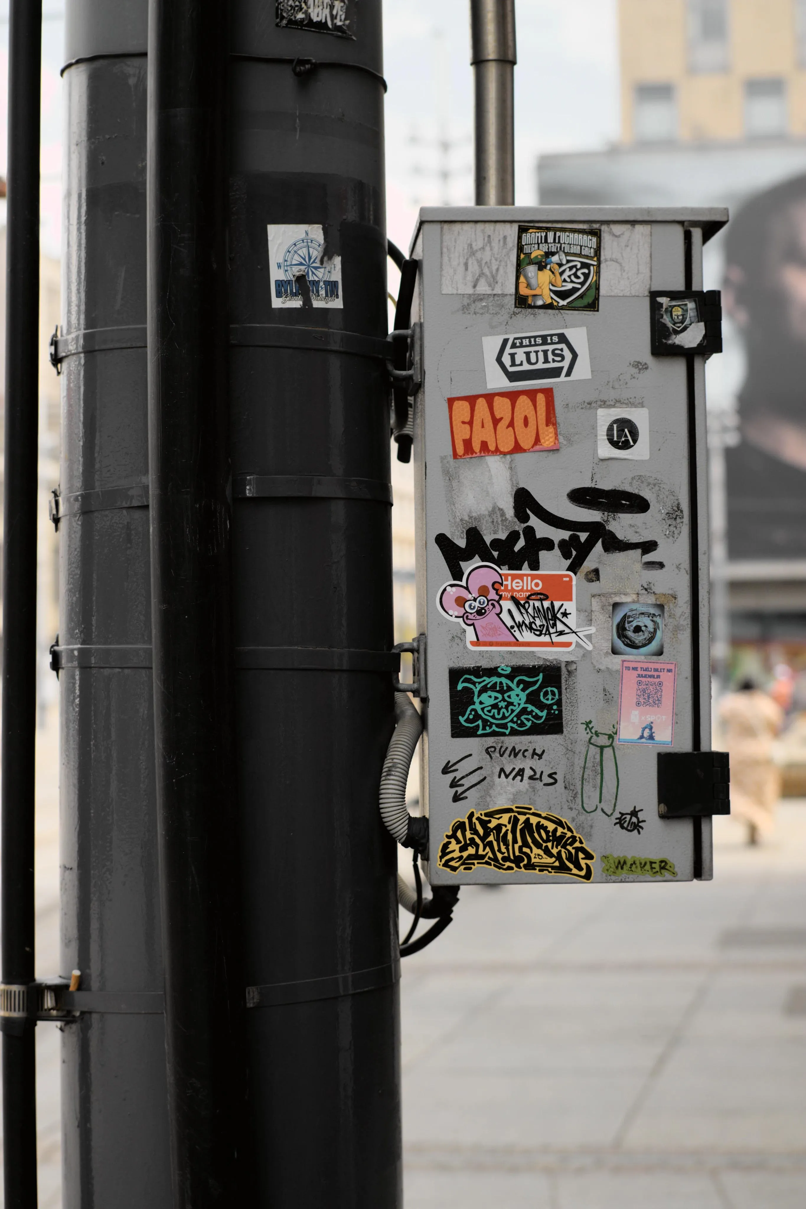 A photo of a gray utility box attached to a pole with bunch of stickers and writings