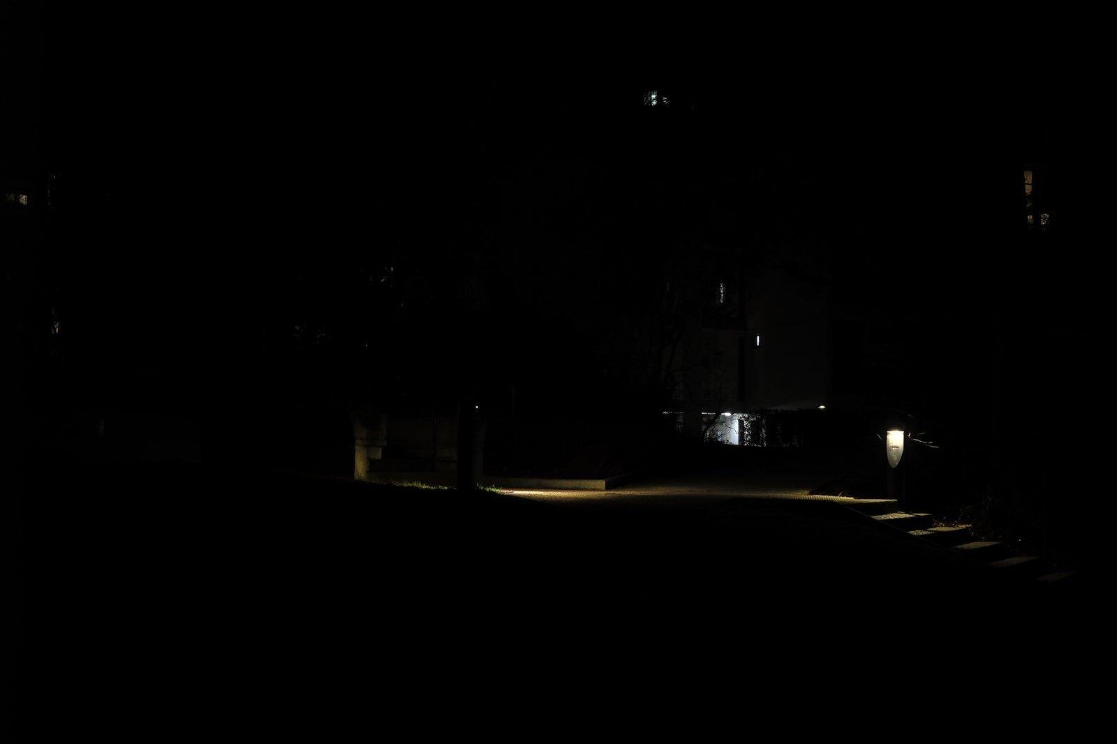 Photo horizontale de nuit. Majoritairement noire, on a des petites lampes éclairant un escalier et son palier