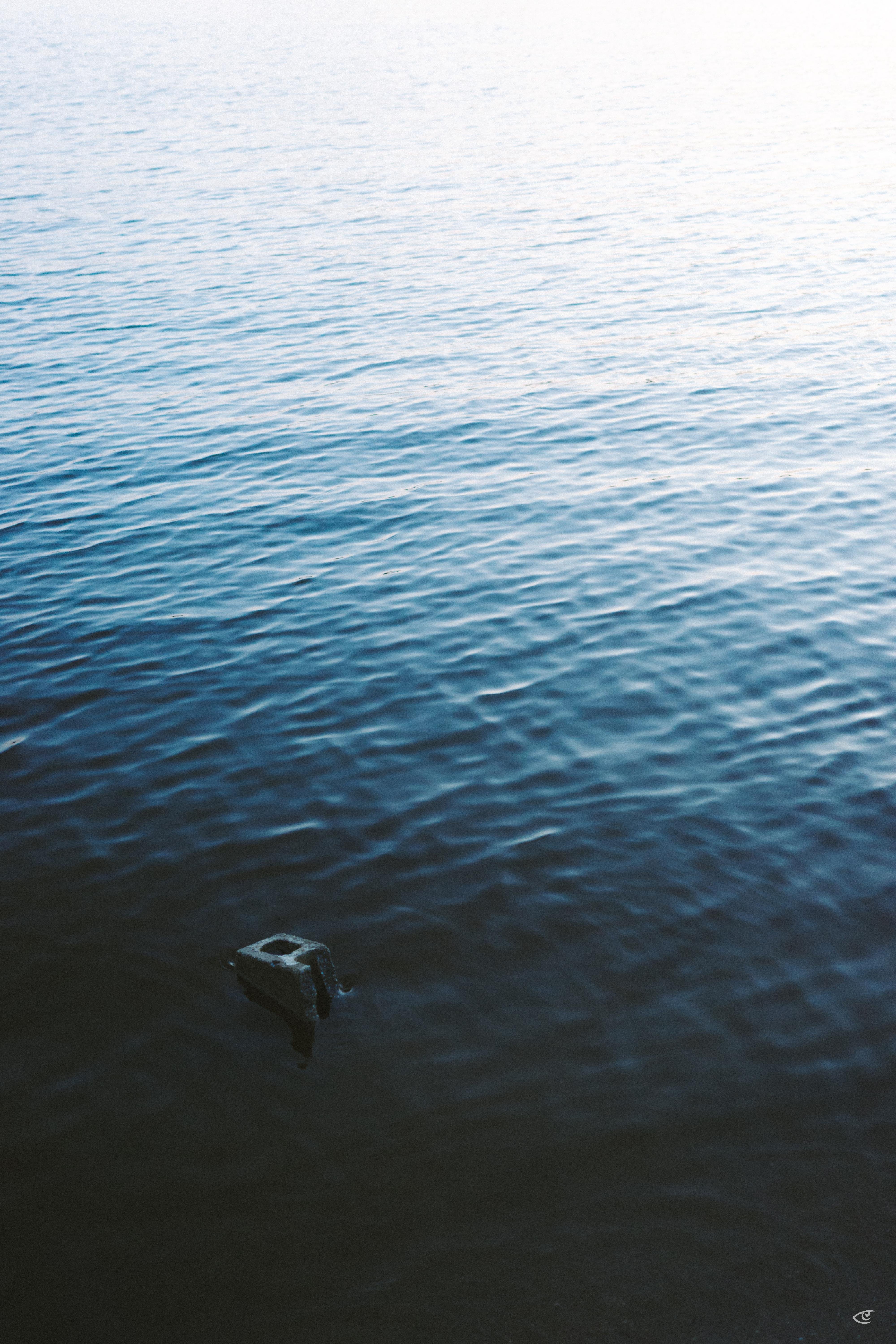 Rippling blue water fills the frame, fading to bright glare near the top; a small dark metal bracket or mooring fixture protrudes from the water near the lower left.
