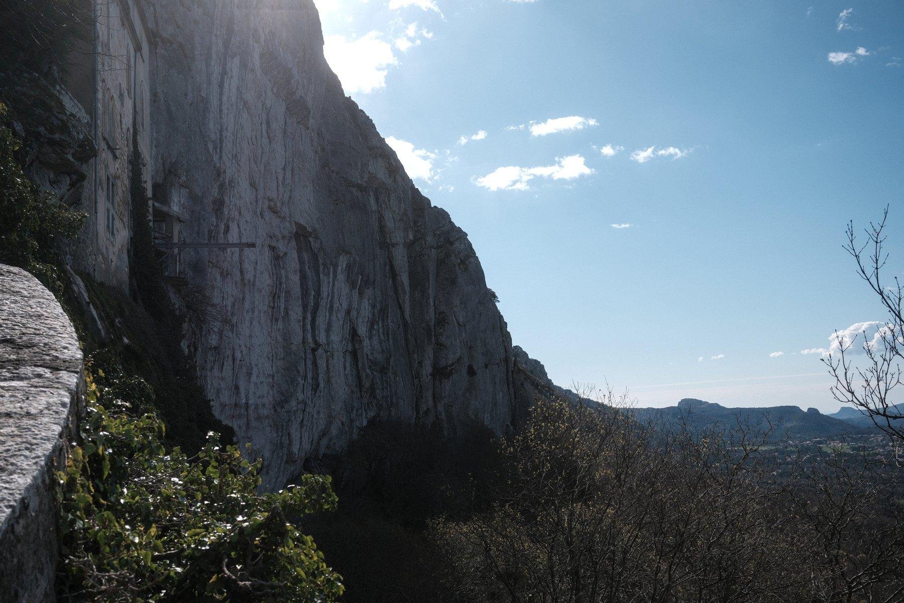 Photo horizontale. Depuis la gauche, une falaise se dessine vers l’horizon et laisse place à un ciel bleu teinté de nuages
