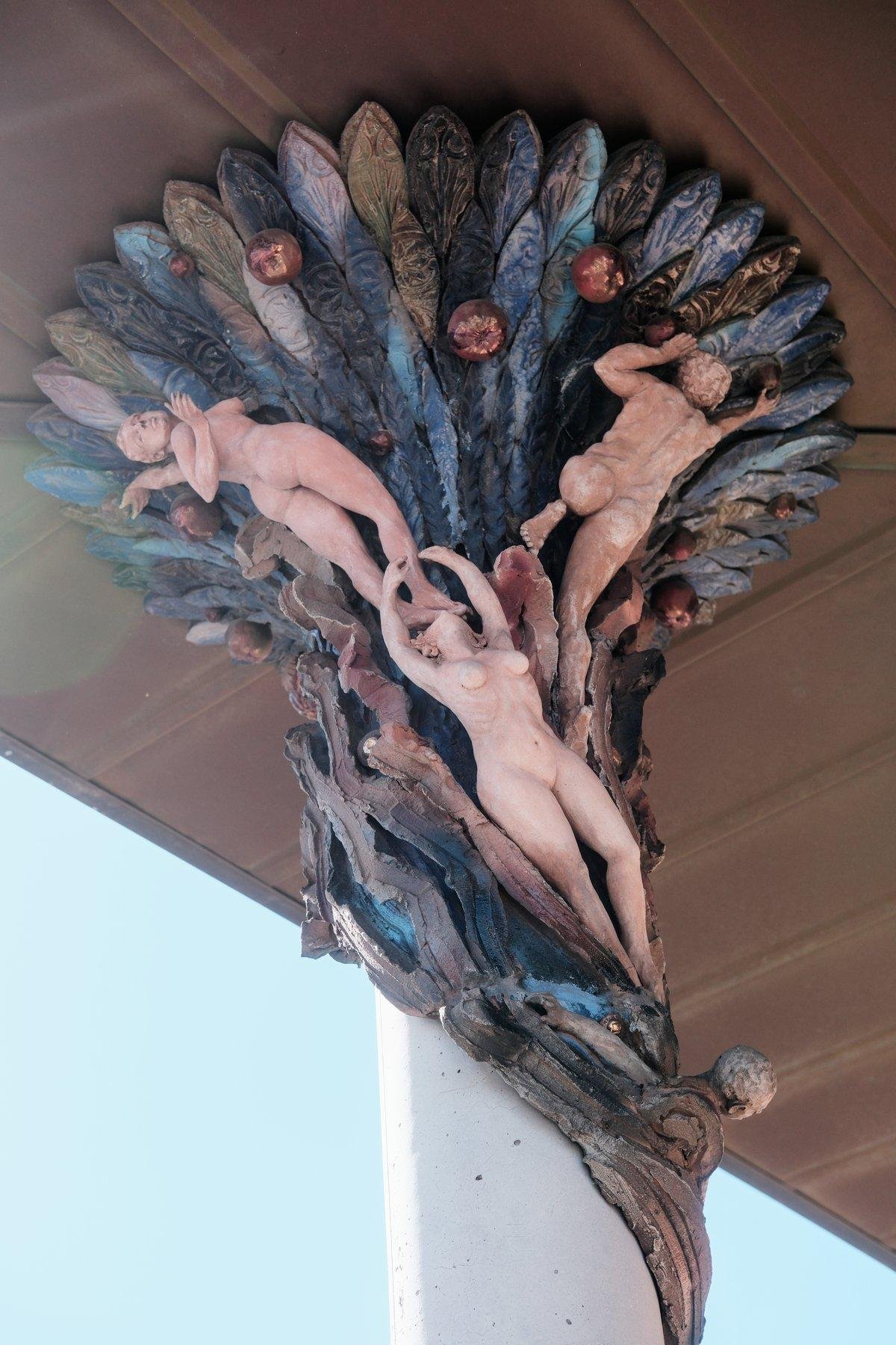 Photo verticale. Décoration de haut de colonne rejoignant le plafond, en extérieur, représentant des femmes nues sur un décors abstrait dans les tons bleutés