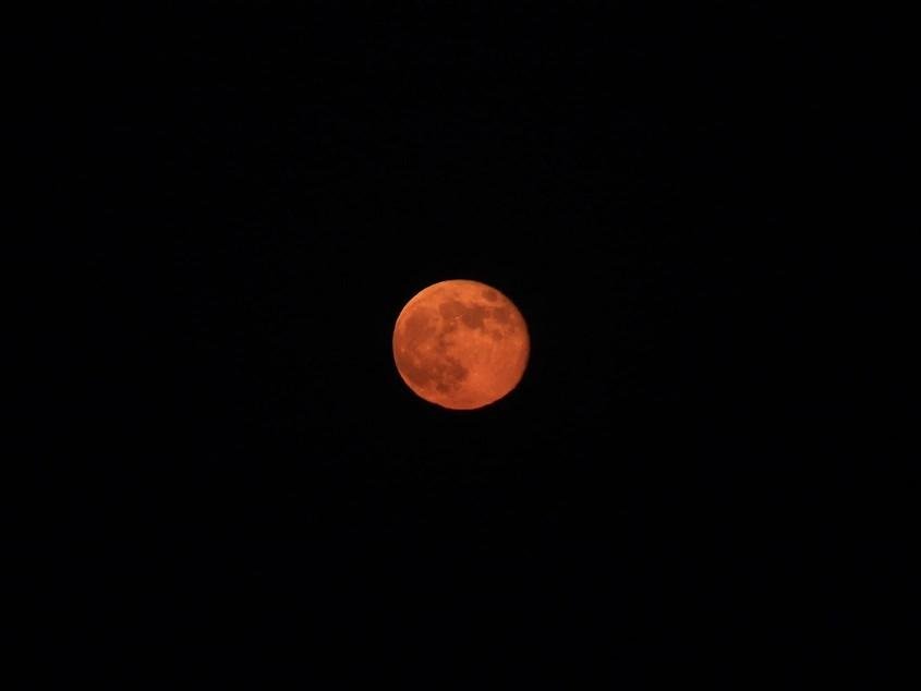 Una fotografía en la que se ve un fondo negro que es el cielo, y una luna casi llena de color rojo y anaranjado, que se ve nítida y en la que se aprecian perfectamente los cráteres