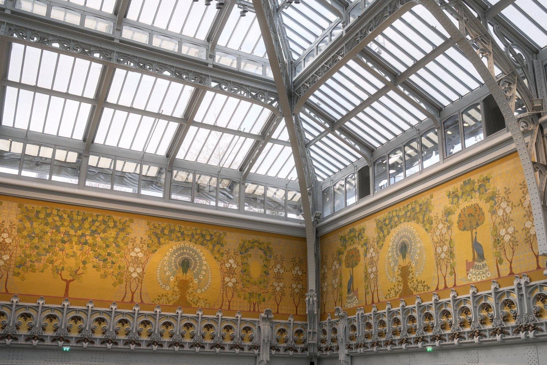 Photo horizontale. Coin de la grande verrière au dernier étage de La Samaritaine. Toutes d’acier et verre, une grande fresque jaune avec des paons et des arbres stylisés