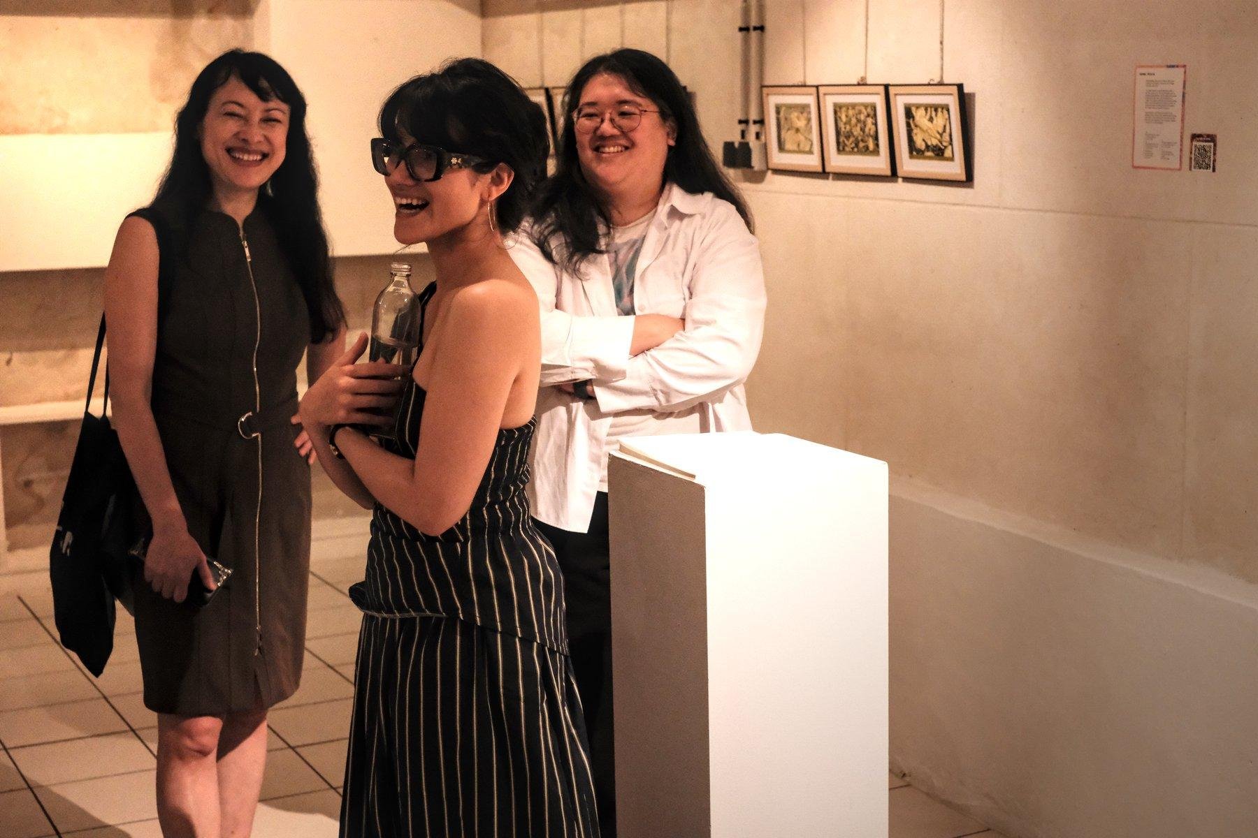 Photo horizontale, dans une galerie d’art, 3 femmes regardent à gauche en riant