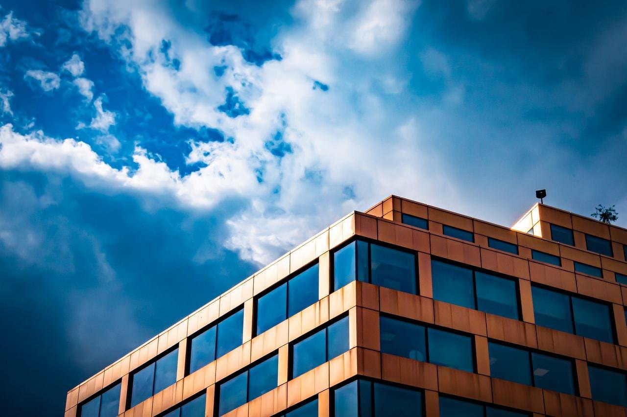 Contemporary building with gold-toned exterior and large glass windows against a dramatic sky filled with both bright blue and dark clouds.