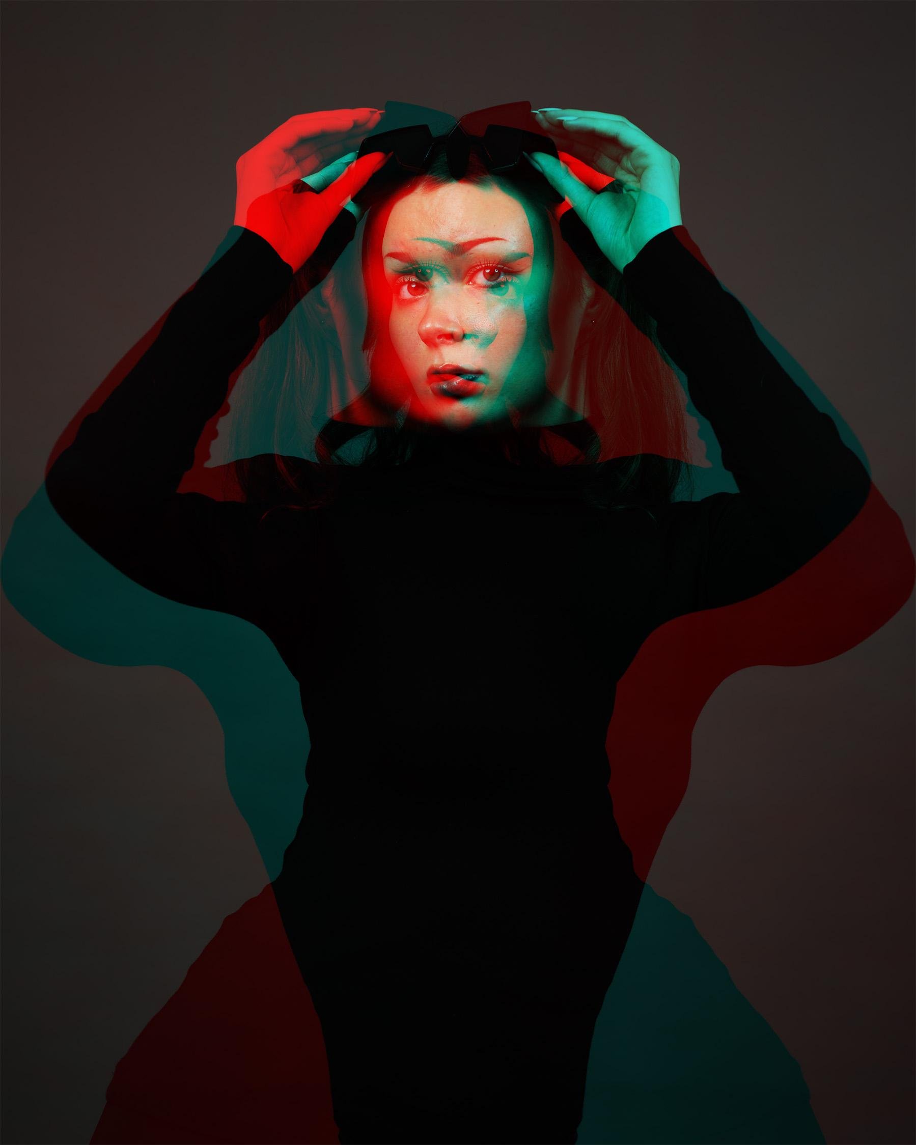 Woman with long hair and a bow on her head, wearing a black top. The image features a double exposure effect with overlapping red and teal layers, creating a ghost-like appearance. The background is dark, enhancing the visual contrast.