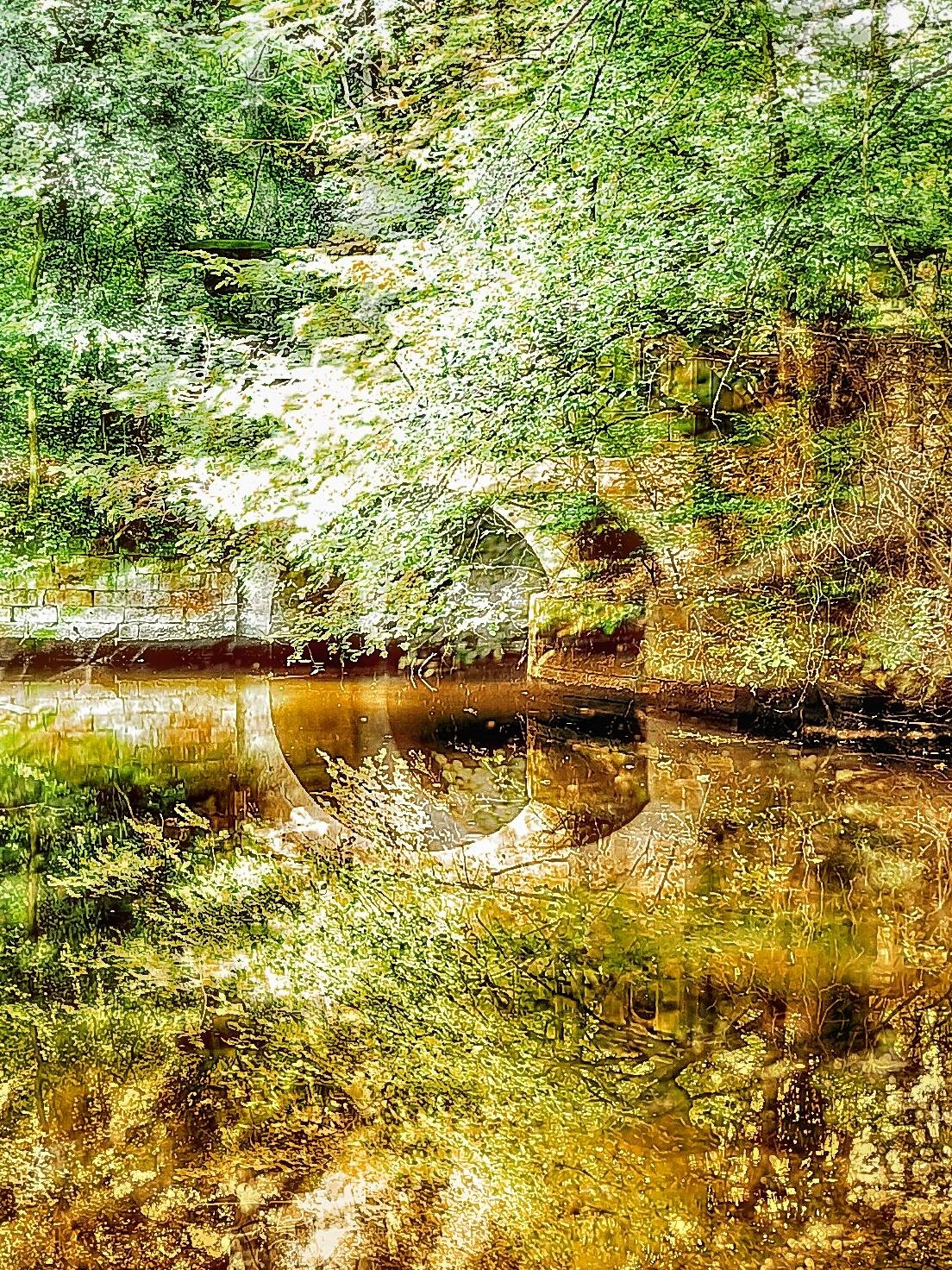 Double exposure style scene: A pond in a wooded area with overhanging branches and a stone bank, overlaid with a large, semi-transparent photograph of a bridge; green foliage and brown water reflections blend together in the image.
###
Szene im Doppelbelichtungsstil: Ein Teich im bewaldeten Gebiet mit überhängenden Ästen und einem steinernen Ufer, überlagert von einer großen, halbtransparenten Aufnahme einer Brücke; grünes Laub und braune Wasserspiegelungen verschmelzen im Bild.