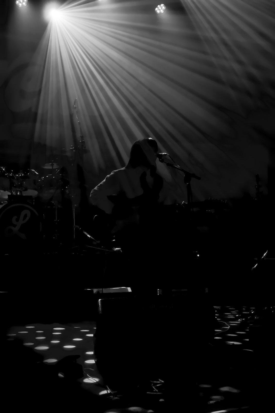 Photo verticale noir et blanc. Une musicienne en contre jour, assise et éclairée par des rayons de lumière