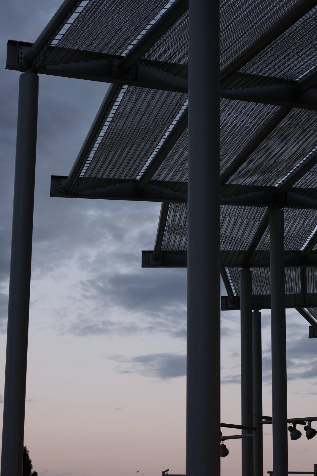 un bout de toit de préau non régulier qui forme un «&nbsp;escalier&nbsp;» circulaire sur le ciel du soleil couchant, avec les poteaux de soutiens