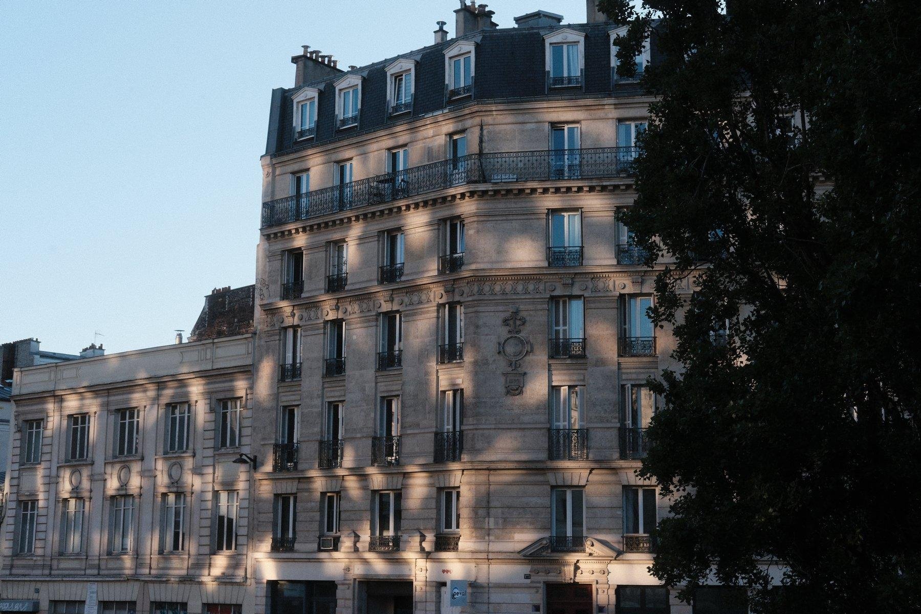 Photo horizontale. Une façade d’immeuble parisien, avec des reflets de lumières qui font penser à des reflets d’eau