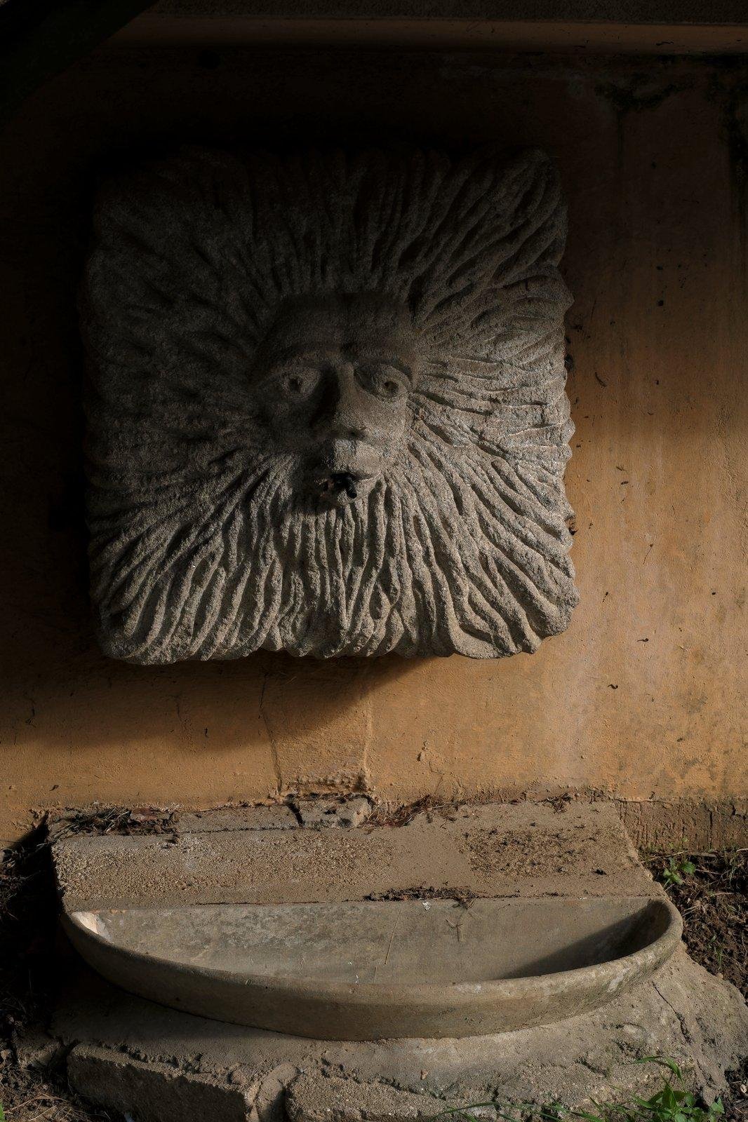 Photo verticale. Une petite fontaine à tête de Lion stylisée dans un carré