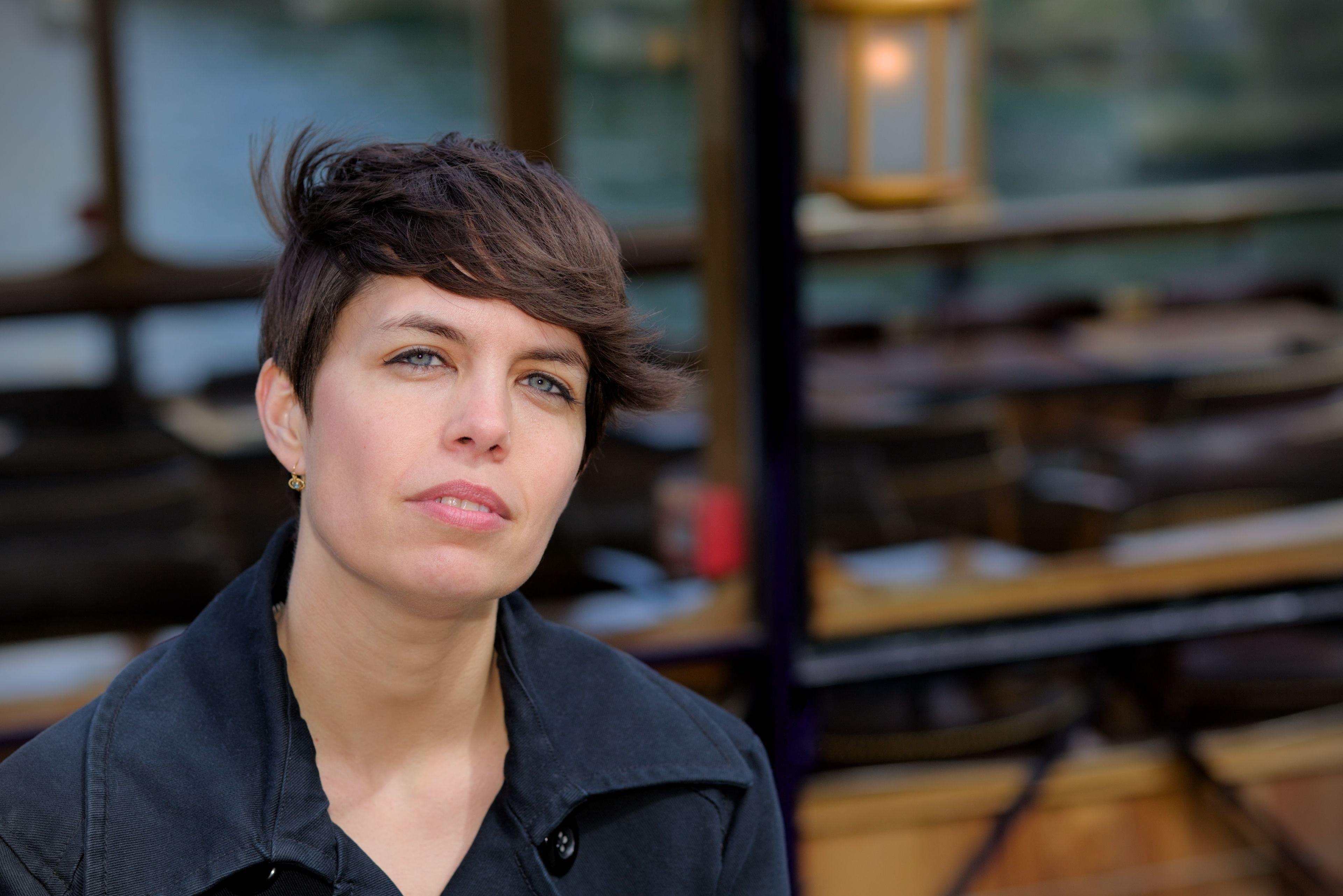 Une brune au centre de la photo, cheveux courts, le visage tourné vers la caméra. Un bout de péniche avec du bois en fond