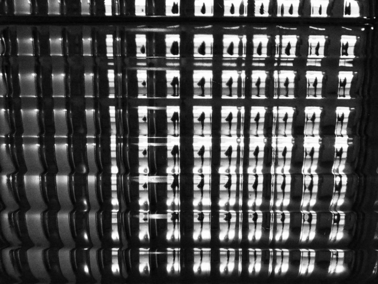 Soggetto umano impossibile da identificare, ritratto attraverso una mattonella di vetro che ne moltiplica l'immagine come attraverso una sorta di prisma. Foto in bianco e nero.