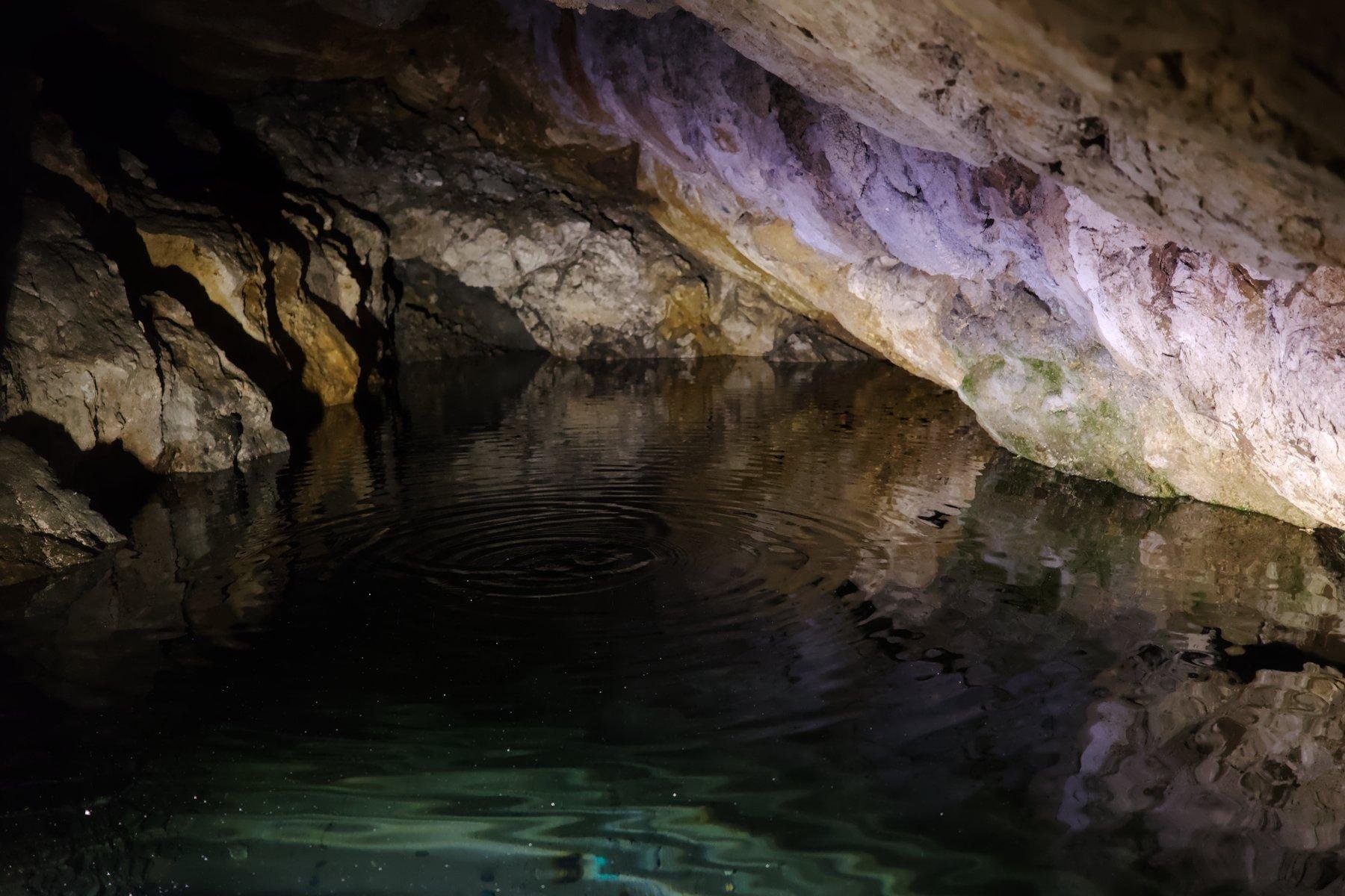 Photo horizontale. Une petite source d’eau dans une grotte sous une cavité de roche