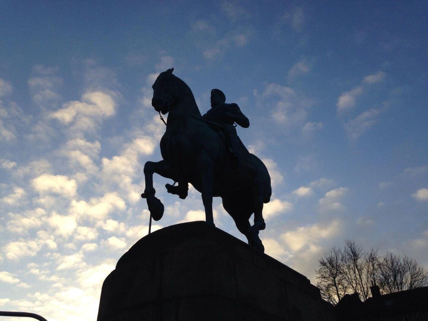 Das Kaiser Friedrich Denkmal in Aachen von unten aufgenommen. Man kann einige Baumkronen im Hintergrund erkennen und den blauen Himmel mit einigen weißen Wolken.