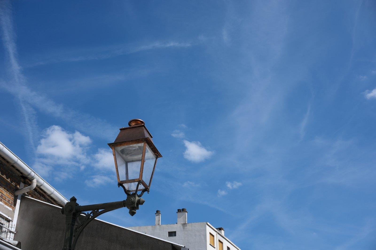 le haut un lampadaire ornementé, sur un fond de ciel bleu strié de volute de nuages