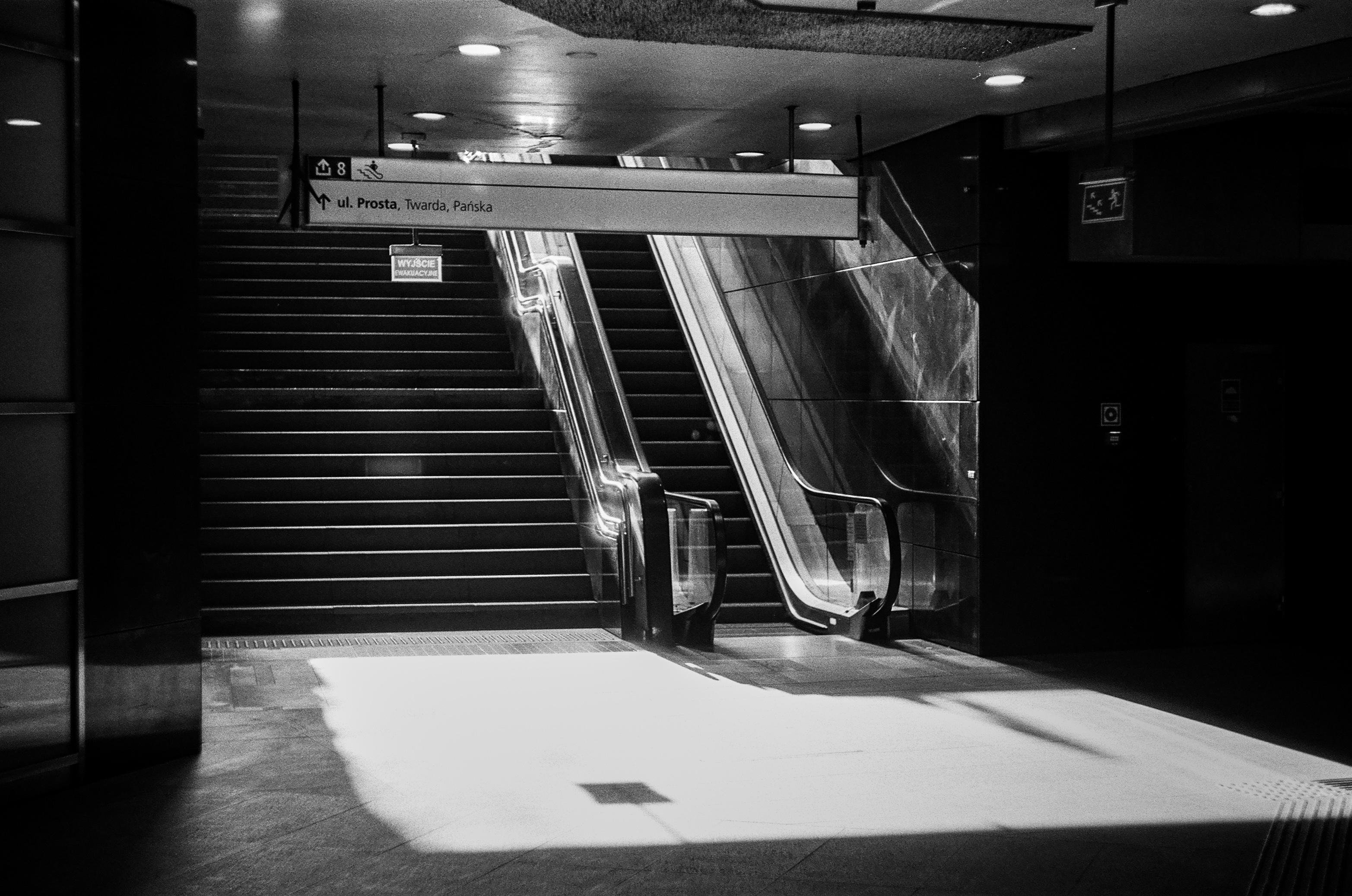 B&W grainy film photo of a stairwell and escalator out of a metro station