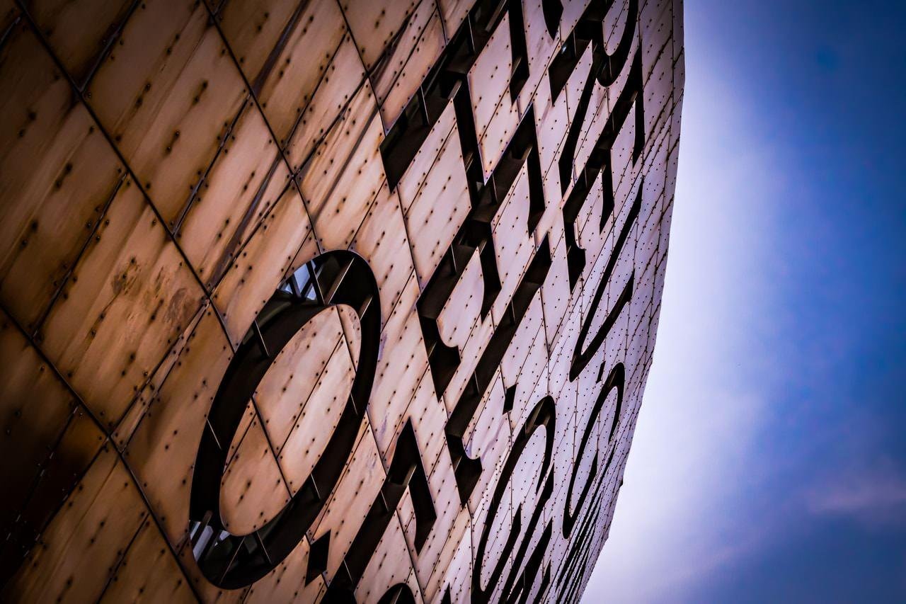 This image shows part of the Wales Millennium Centre in Cardiff, Wales. The building is known for its distinctive facade, which features large letters of a bilingual inscription. The material appears to be copper-colored metal panels.