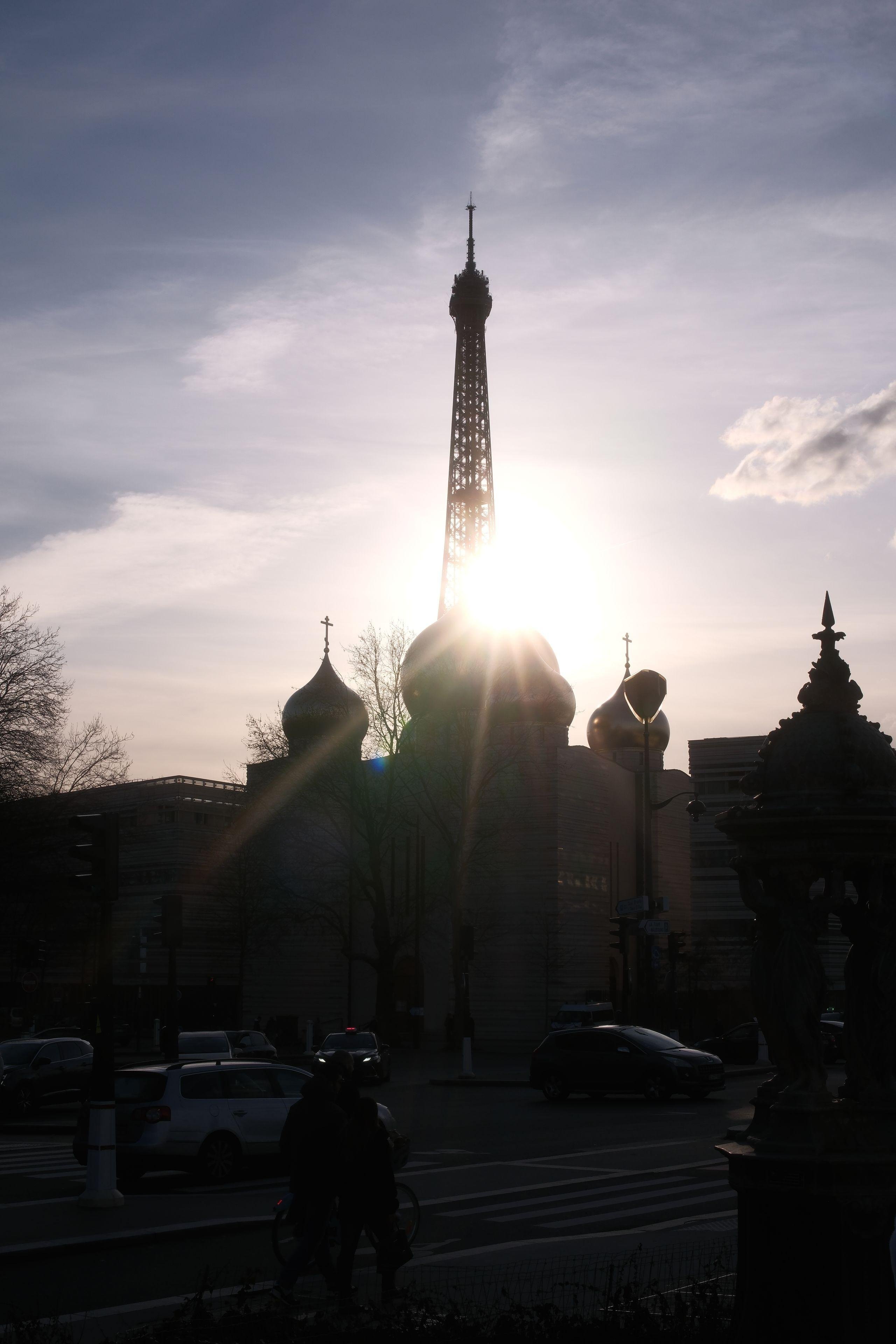 Photo verticale. Le haut de la tour Eiffel en contre jour, et la silhouette de toits d’architecture Russe en contre jour aussi