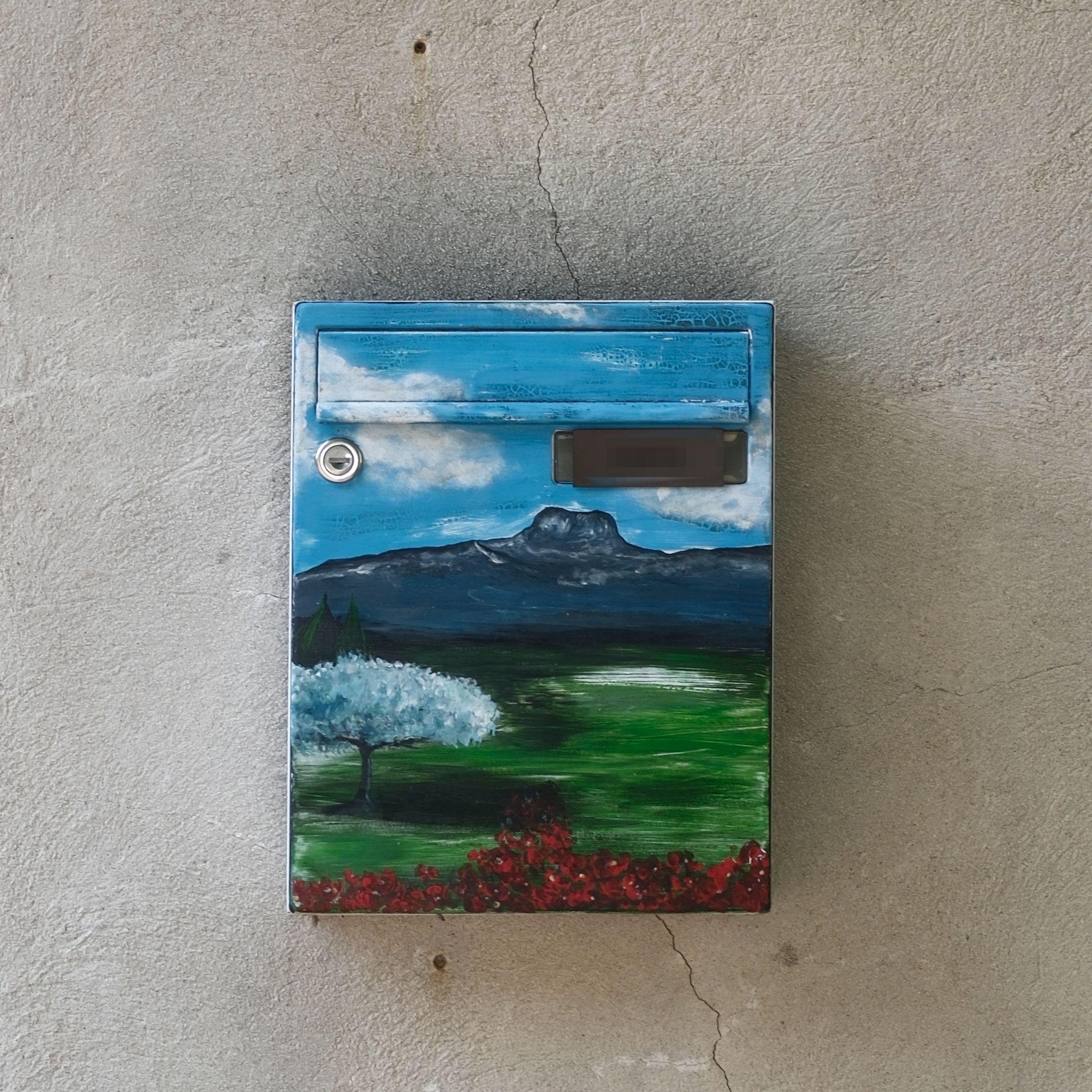 A mailbox, totally painted with a landscape of a plain with a mountain in the background, a tree with white leaves and some red leaves at the front of the paint