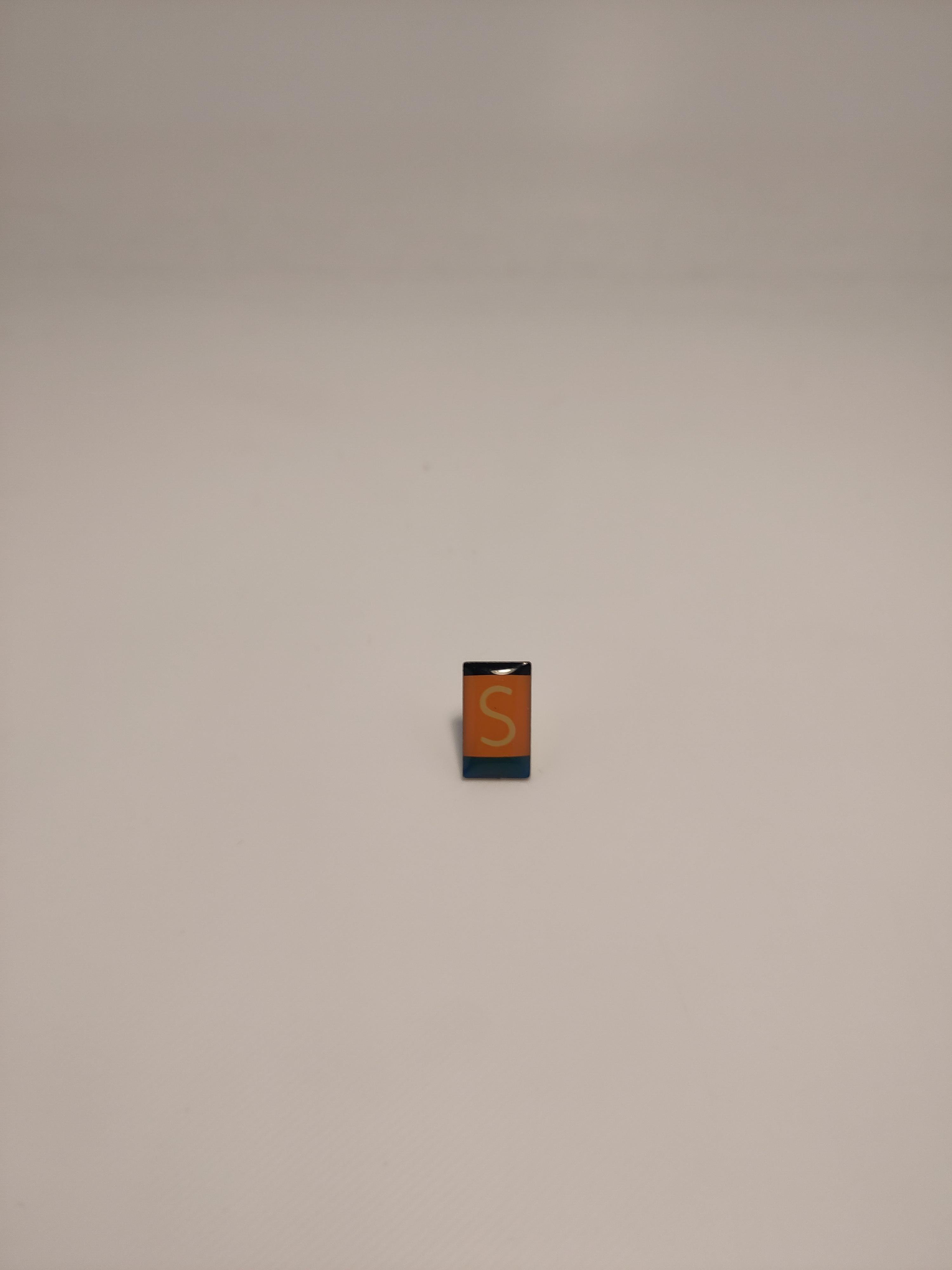 A enemal pin the logo of the Saarbahn.

The logo is a rectancle with a thin black stripe on the top, a big orange rectangle with a white 'S' in the middle, and a thick blue stripe at the bottom