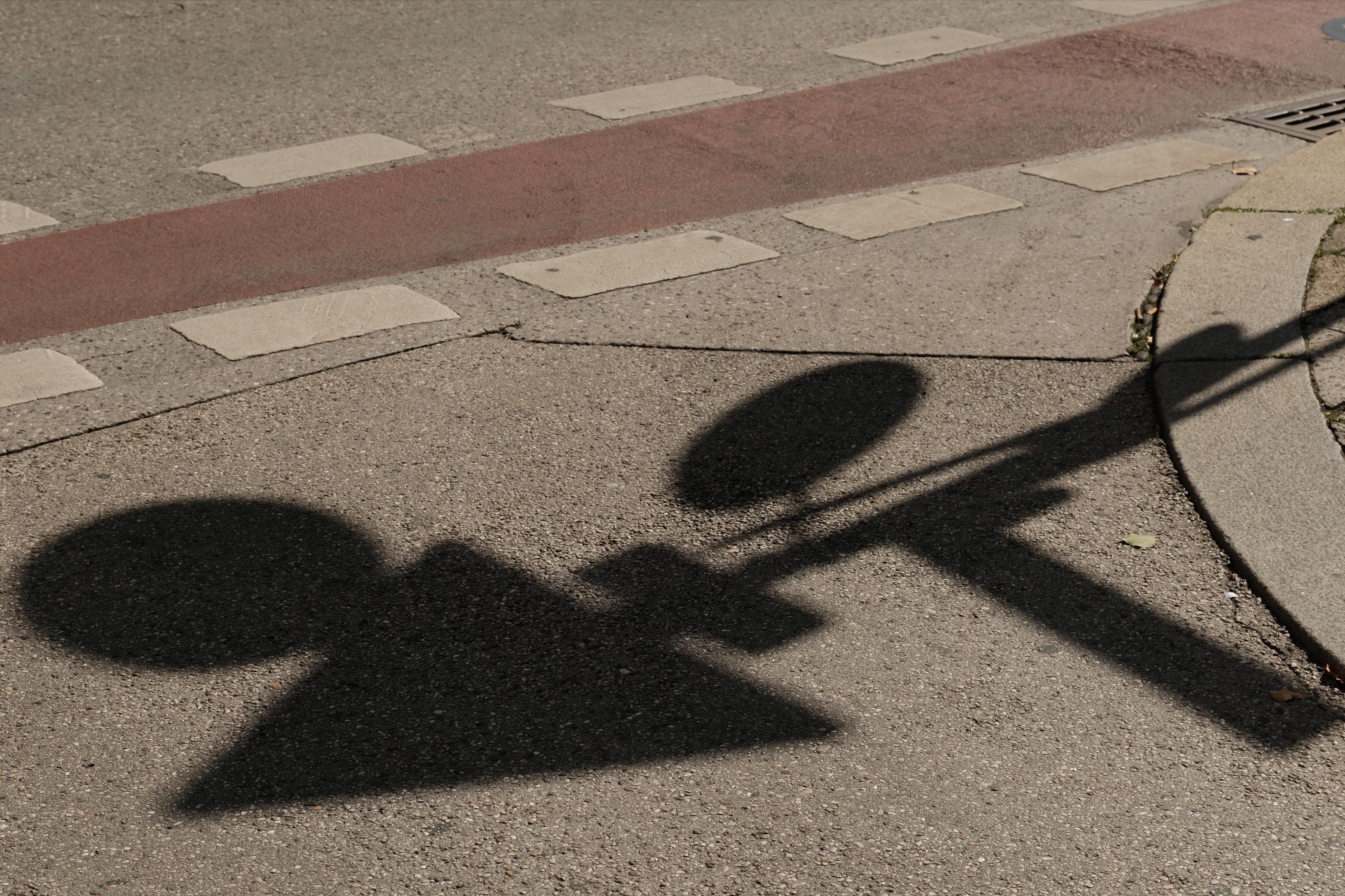 Skewed perspective of a street surface with gray asphalt and a n red and white bike lane. Shadow of a post with several traffic signs pointing in different directions.