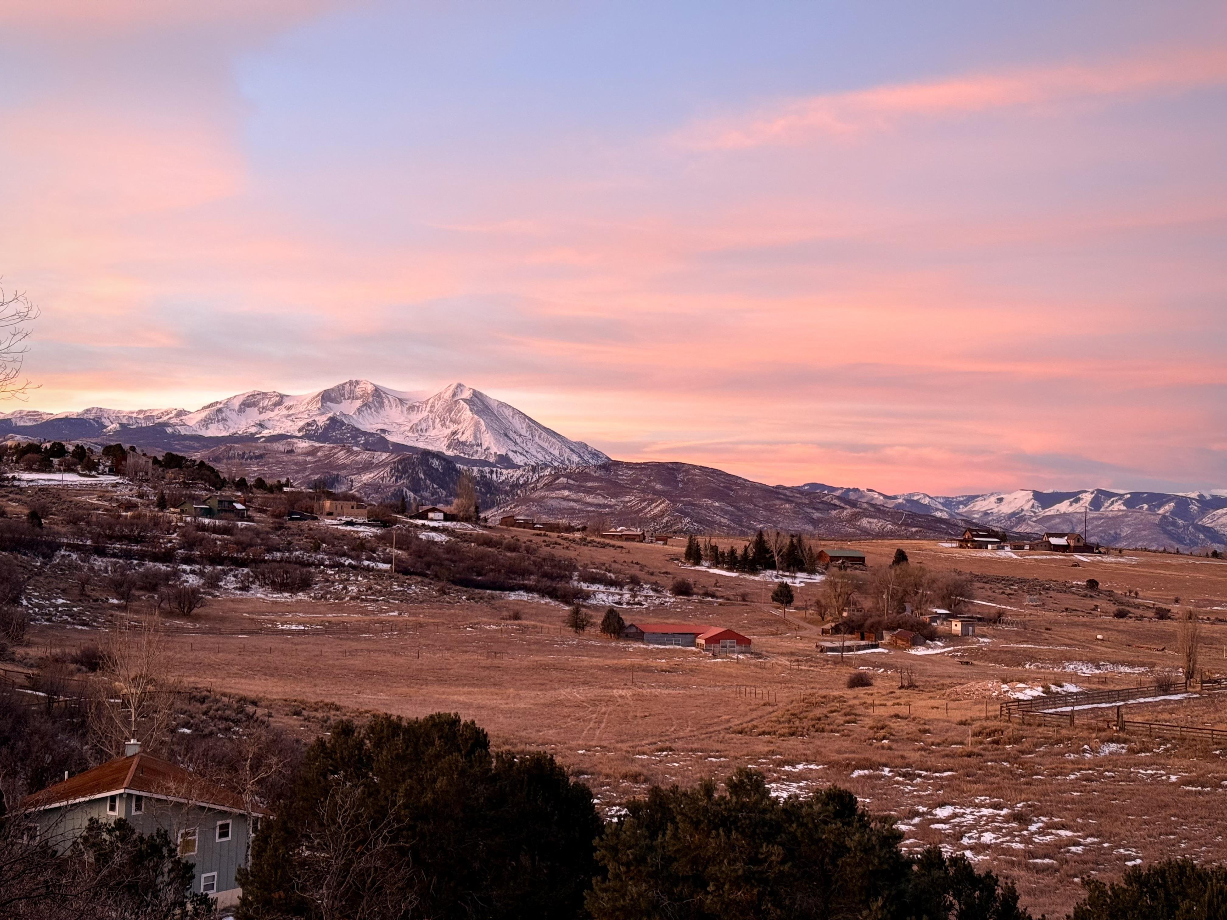 A beautiful view of Mount Sopris after fresh snow. Clouds, a view across fields, a few houses, onto the mountain. A foot or more snow covering everything.