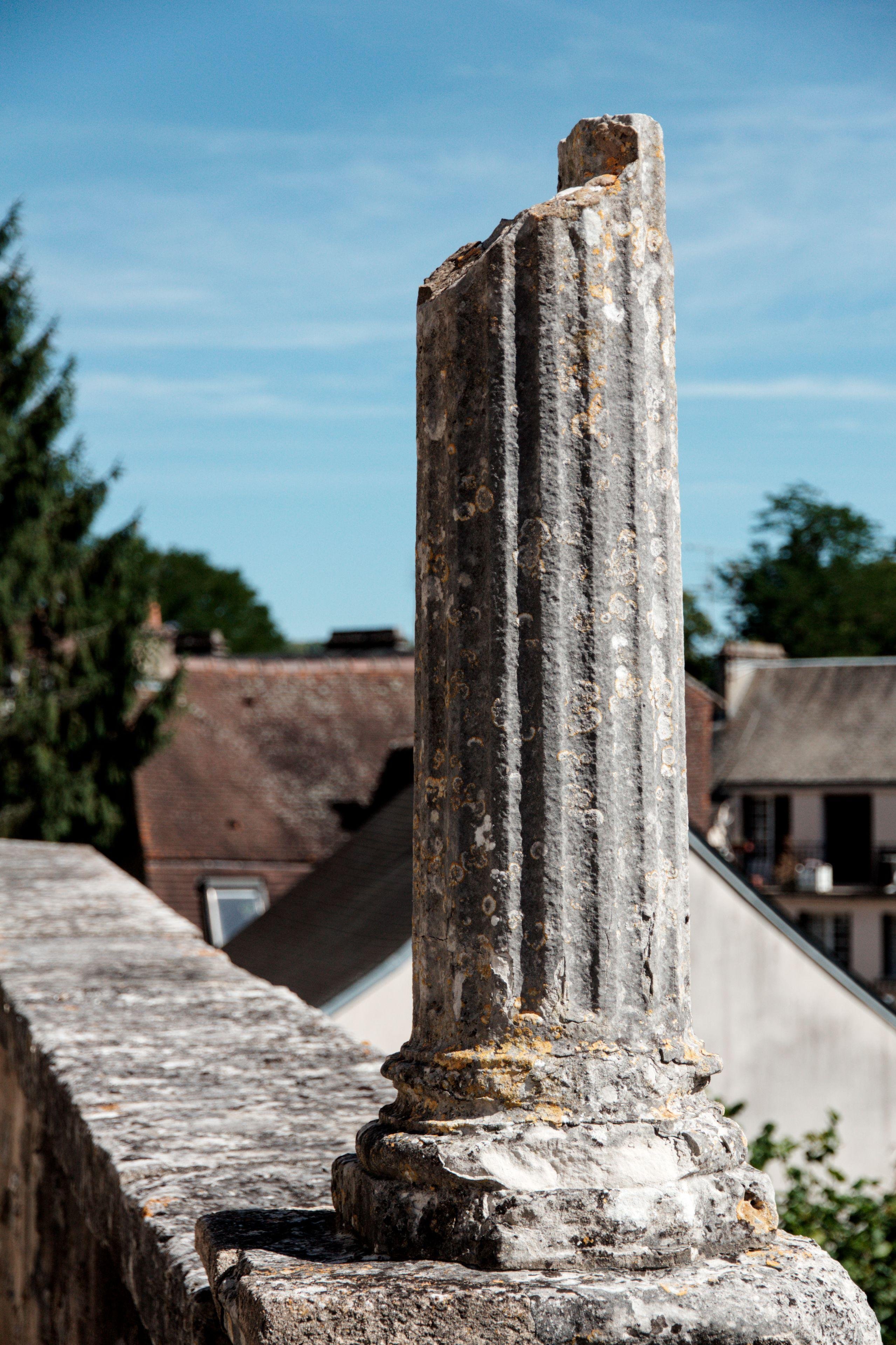 Photo verticale. Une vieille colonne brisée sur un muret sous un ciel bleu avec des nuages