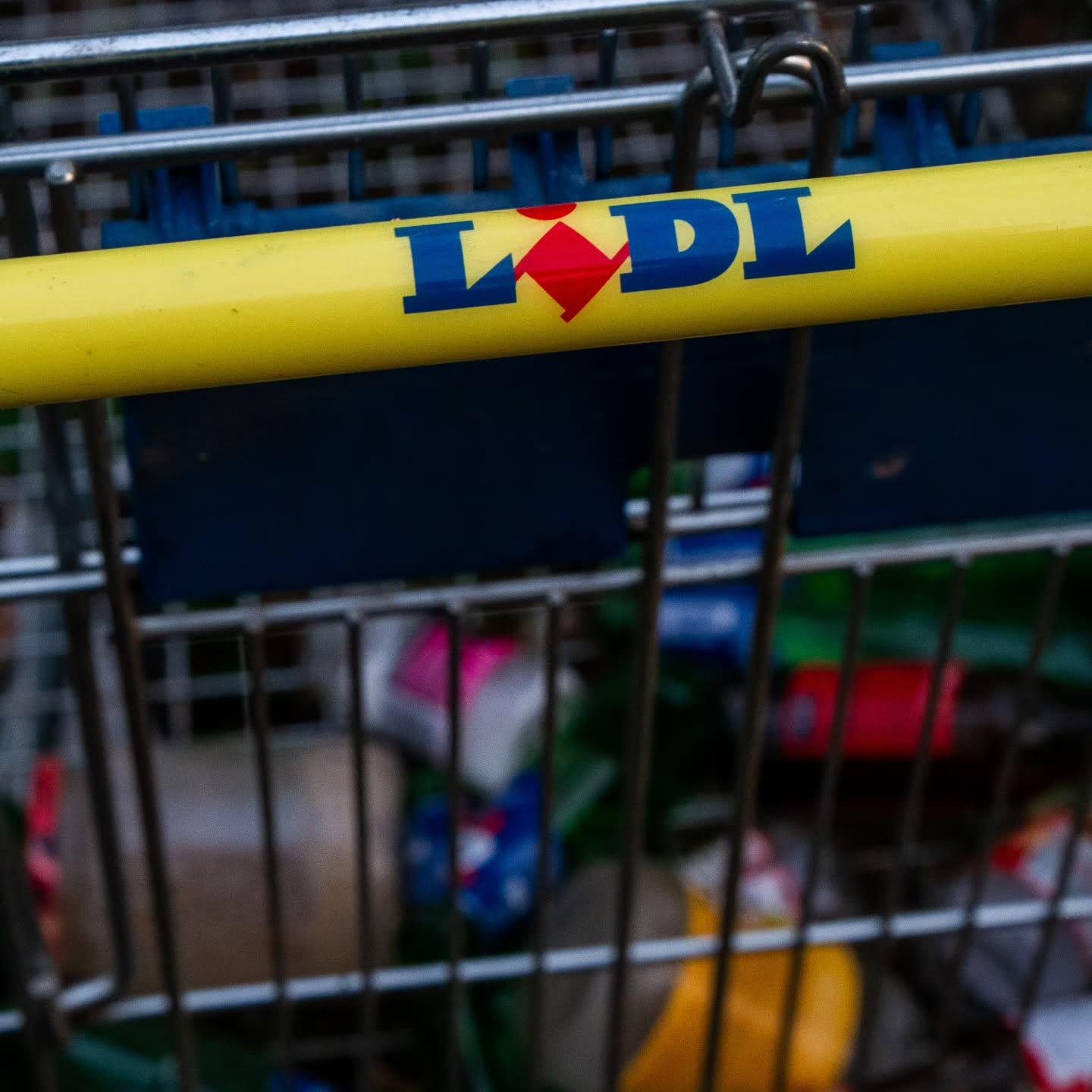 The image shows a shopping cart with the "Lidl" logo on the handle. Inside the cart, there appear to be various rubbish items, though they are not clearly identifiable.