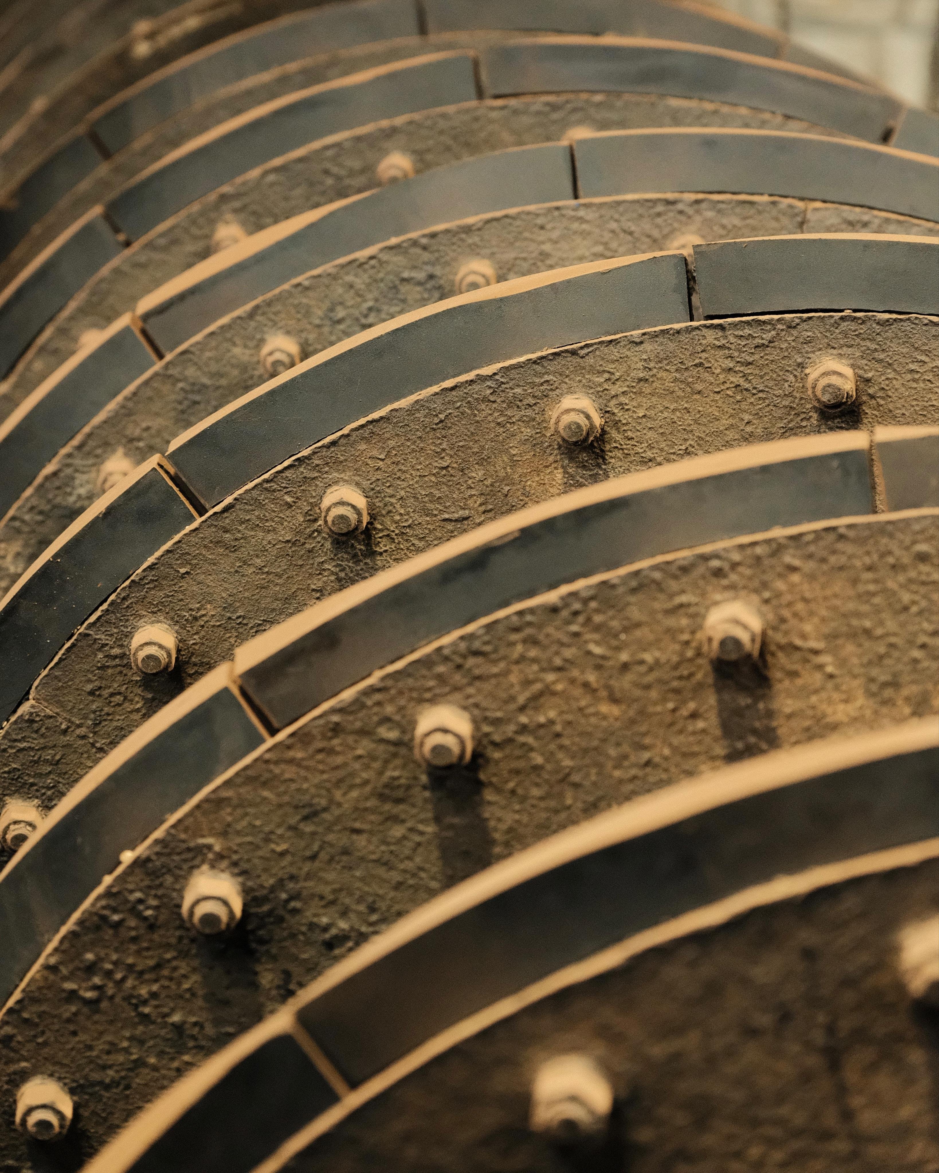 Close-up of ridges on a stone crushing rotary drum, as seen in a mining museum. The section shows multiple layers of metal ridges, which go around the whole barrel; here you can only see about a quarter of the barrels circumference. There are thick bolts holding the metal plate together.