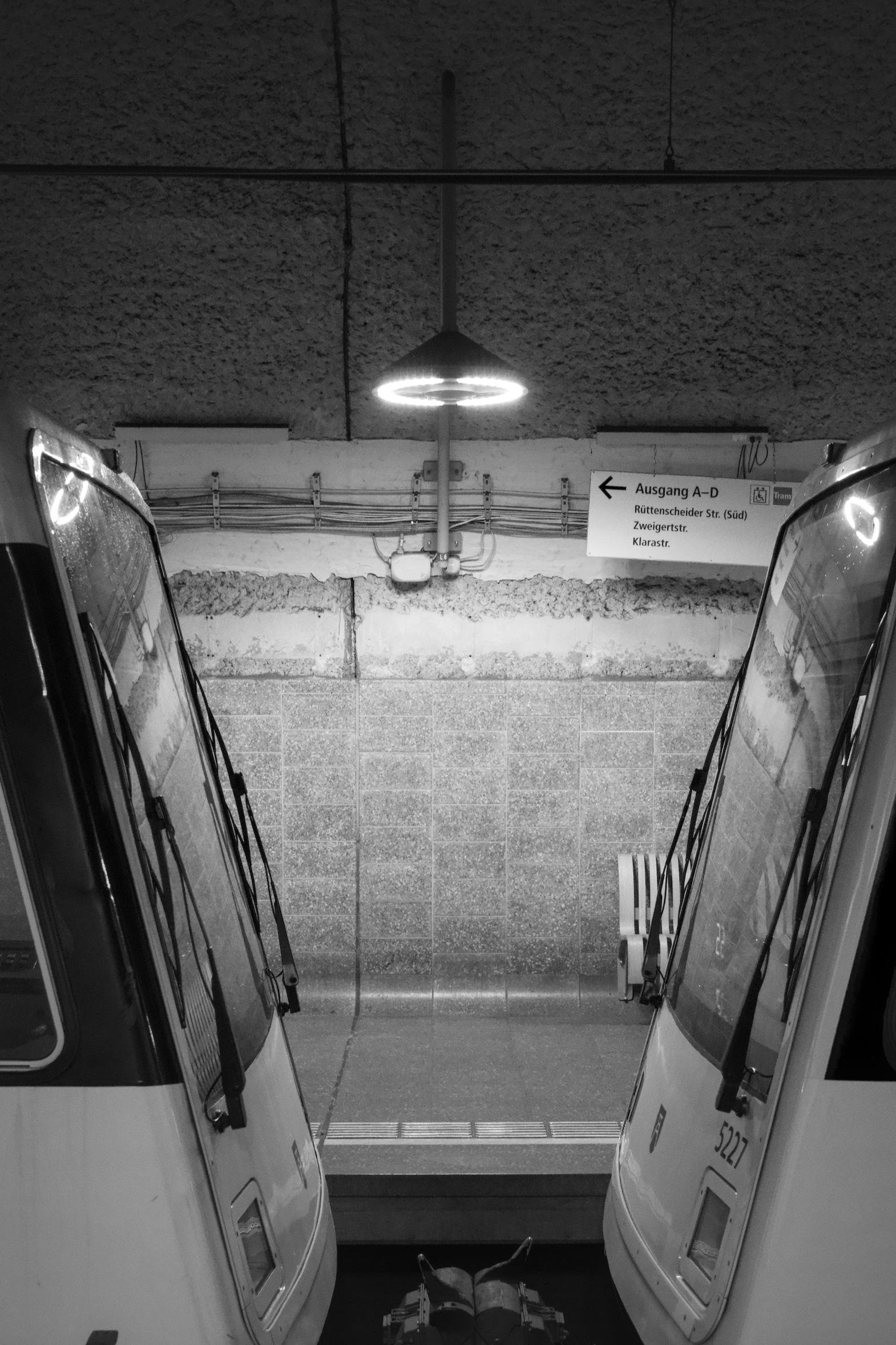 An underground station with two coupled trains. Between them hangs a lamp that reflects in both train windshields. 