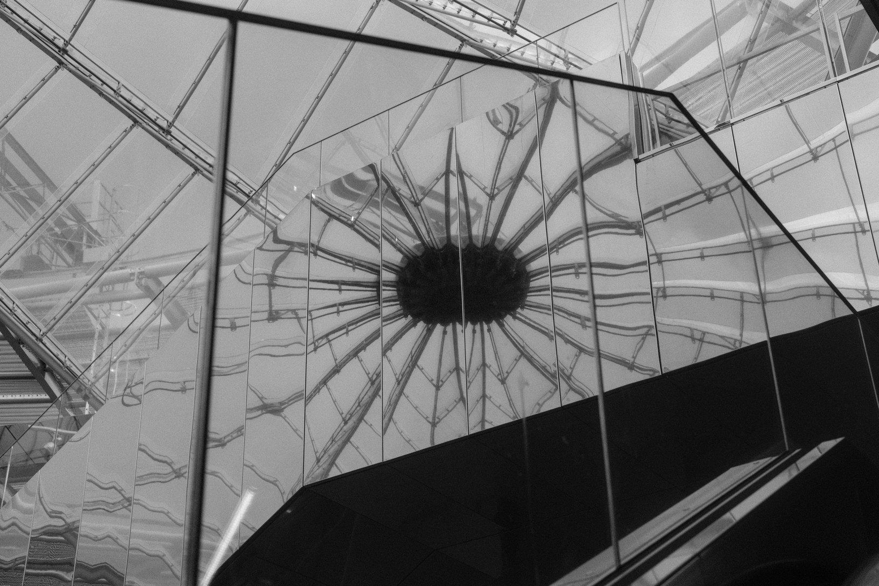 Photo horizontale en noir et blanc. Des plaques de métal polie réfléchissant un gros disque noir dont partent plein de rayons.
