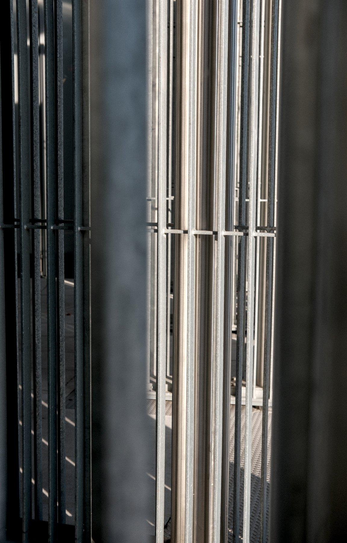 Photo verticale. Vue à travers une grille aux barreaux verticaux, d’autres grilles identiques, la vue n’est que barreaux, du coup