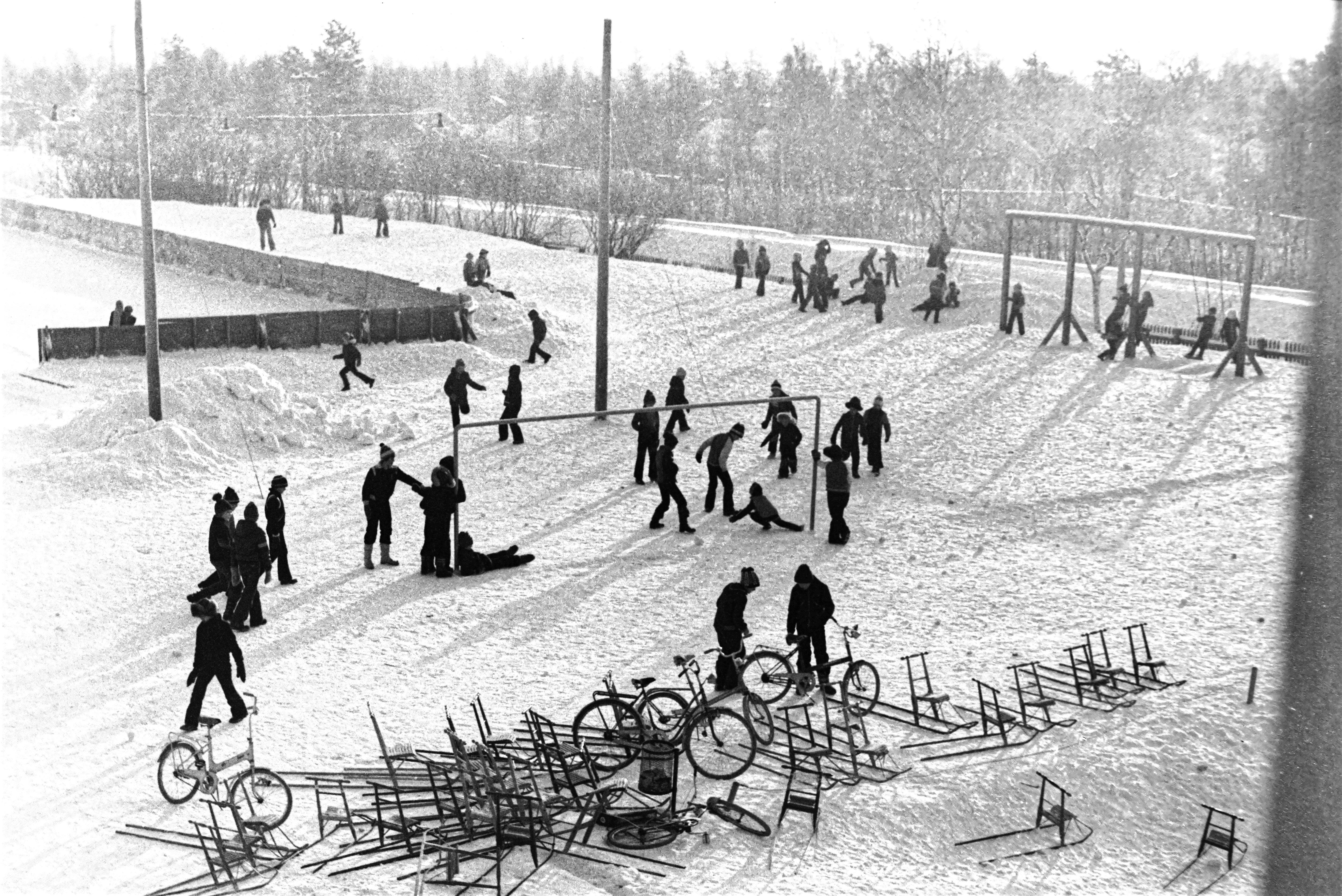 Barn på snötäckt skolgård, parkerade cyklar och sparkstöttingar.