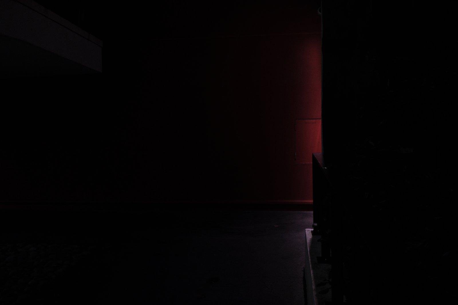 Photo format paysage, de nuit, majoritairement noire, avec juste un halo rouge vertical délimitant le tiers droit de l’image