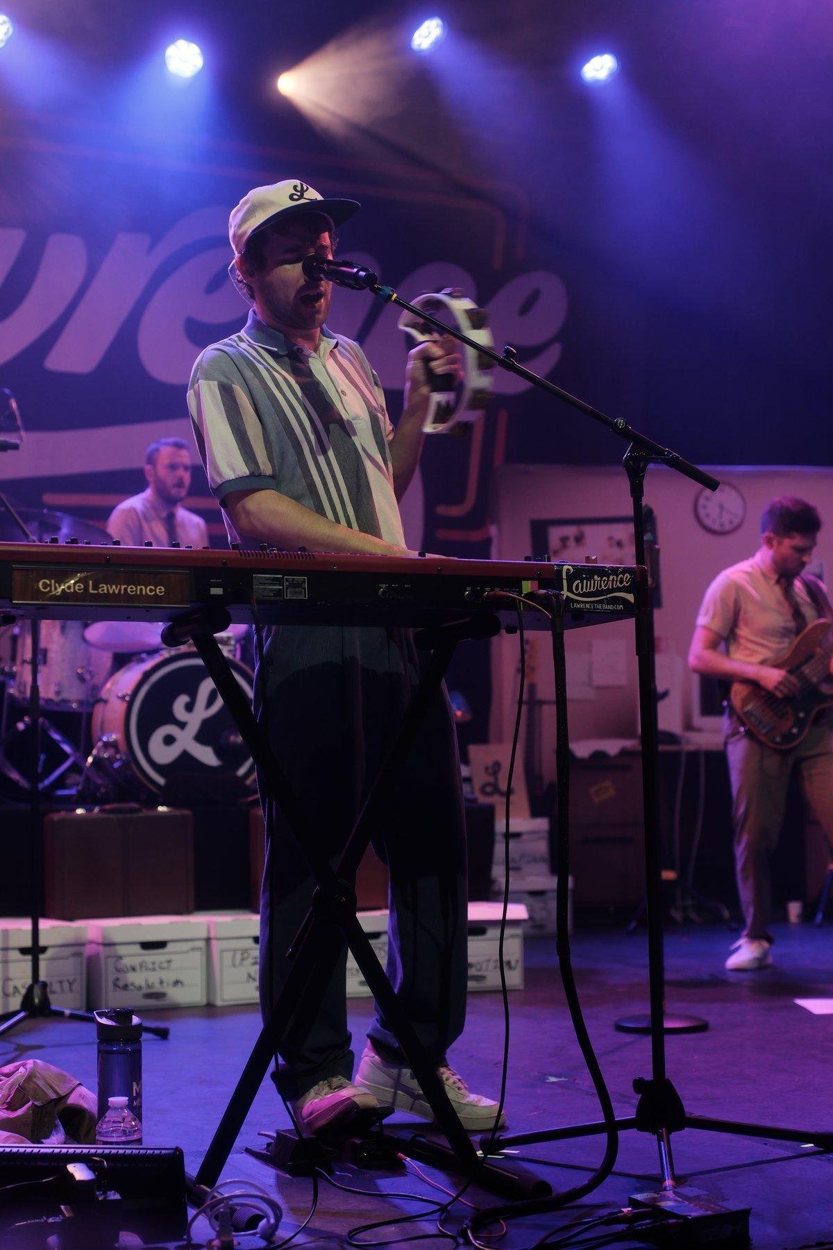 Photo verticale. Clyde Lawrence entrain de jouer du clavier de la main droite et agitant un tambourin de la main droite
