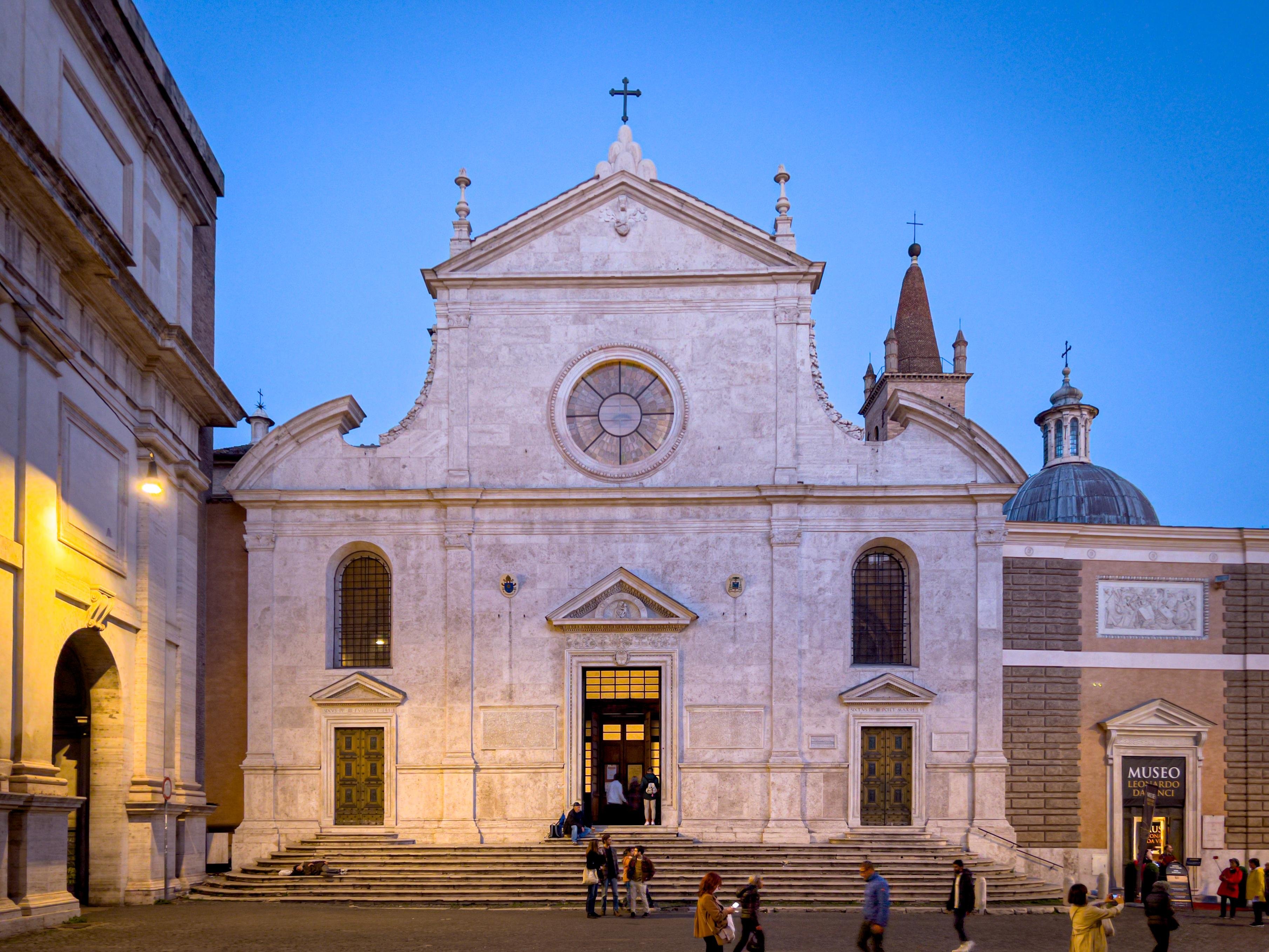 Basilica di Santa Maria del Popolo a Roma, Italia. È una chiesa in stile rinascimentale situata in Piazza del Popolo, nota per la sua facciata intricata e l'importanza storica. L'edificio è adornato con elementi classici come colonne, archi e una finestra circolare centrale. La scena mostra persone all'esterno, evidenziando il suo status di popolare destinazione turistica.