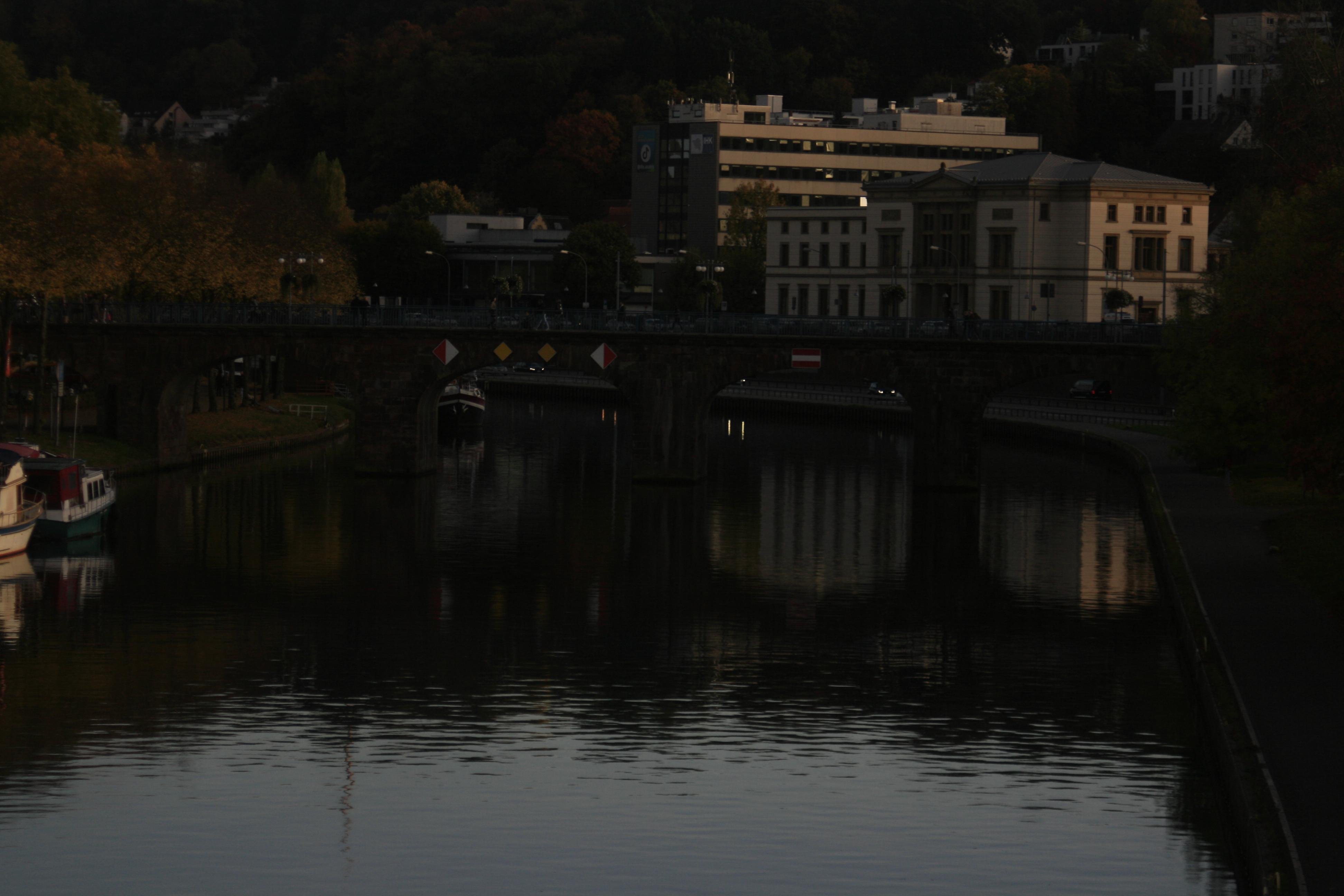 a grey multistory building sitting at the saar with saarbrücken's stadtautobahn in front of it