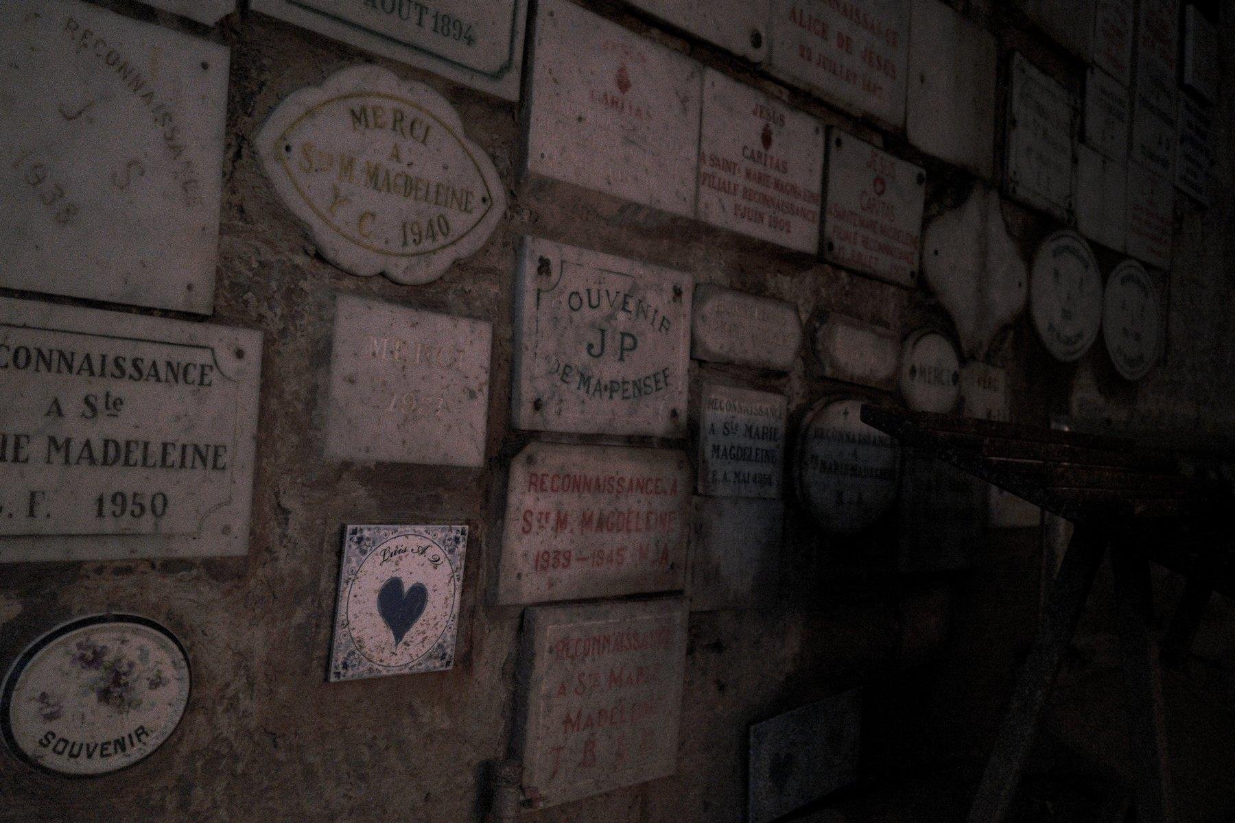 Photo horizontale. Vue sur un mur sur lequel sont posées pleins de plaque en pierre ou céramique, avec un message remerciant l’église