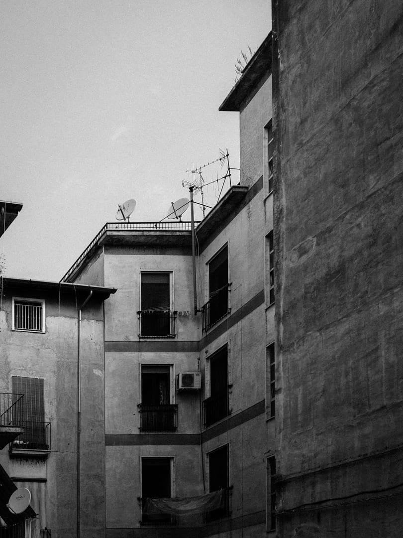 Piani superiori di vecchi palazzi che si affacciano su un cortiletto, ovviamente non visibile nell'inquadratura. Gli elementi dominanti della foto, che è in bianco e nero, sono i balconini e le diverse antenne, convenzionali o paraboliche, montate sia sul tetto che su uno dei balconi.