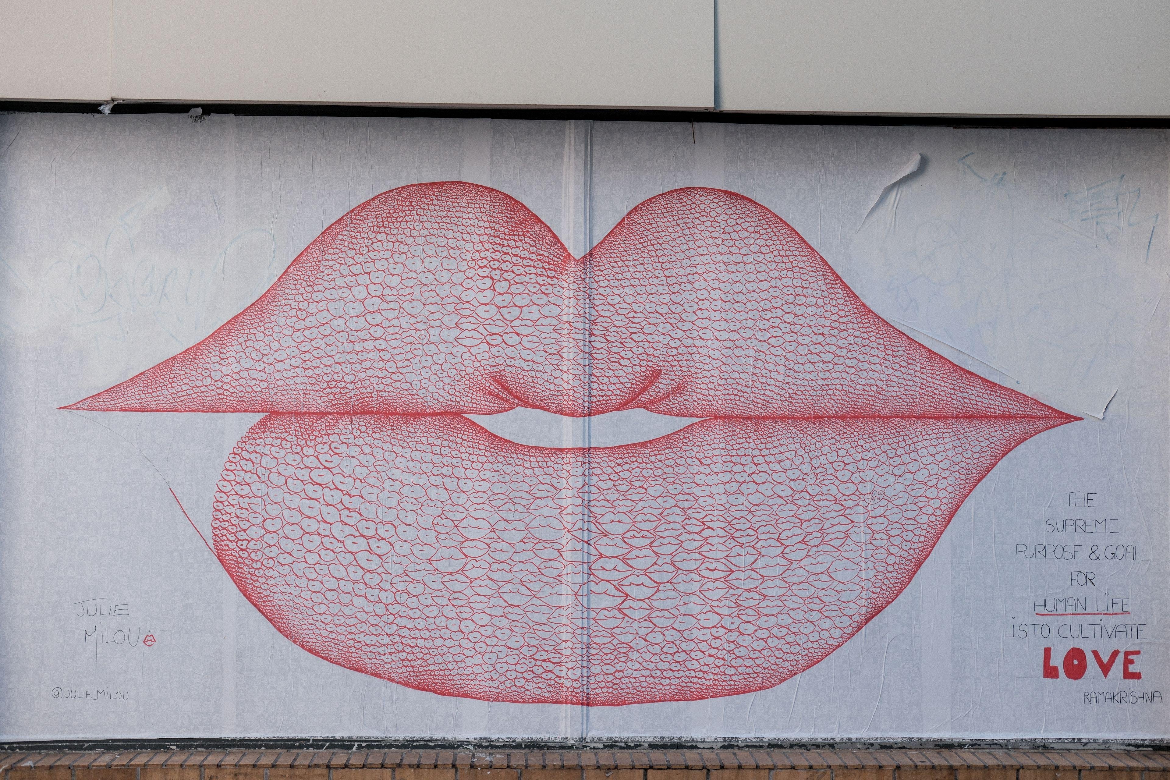 Photo horizontale. Une énorme affiche collée sur un mur, les lèvres de femme dessinées avec plein de mini lèvres